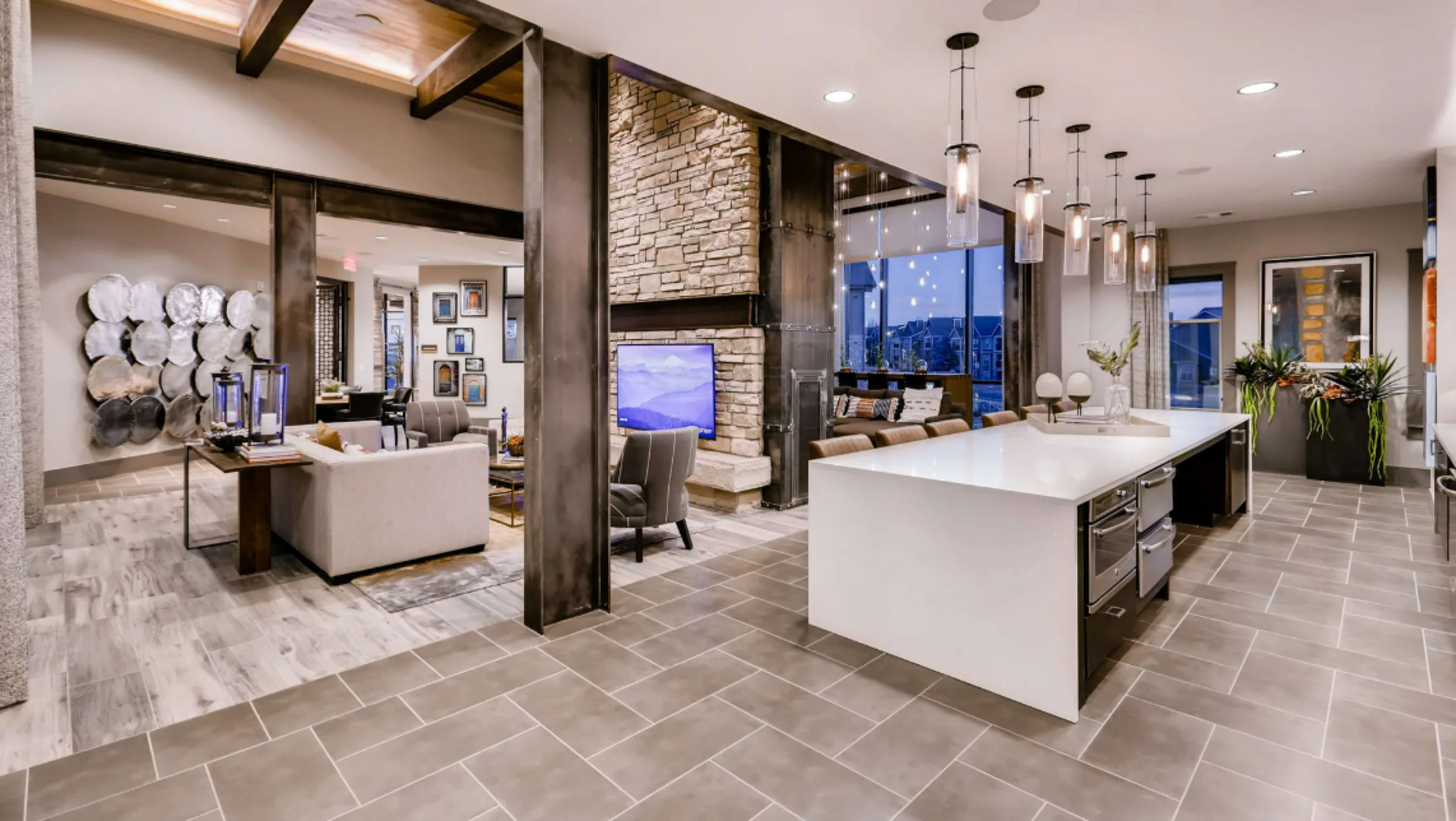 A modern open-concept living space featuring a kitchen with a large island, a cozy seating area, and a stone fireplace, all with large windows offering a view of the city.