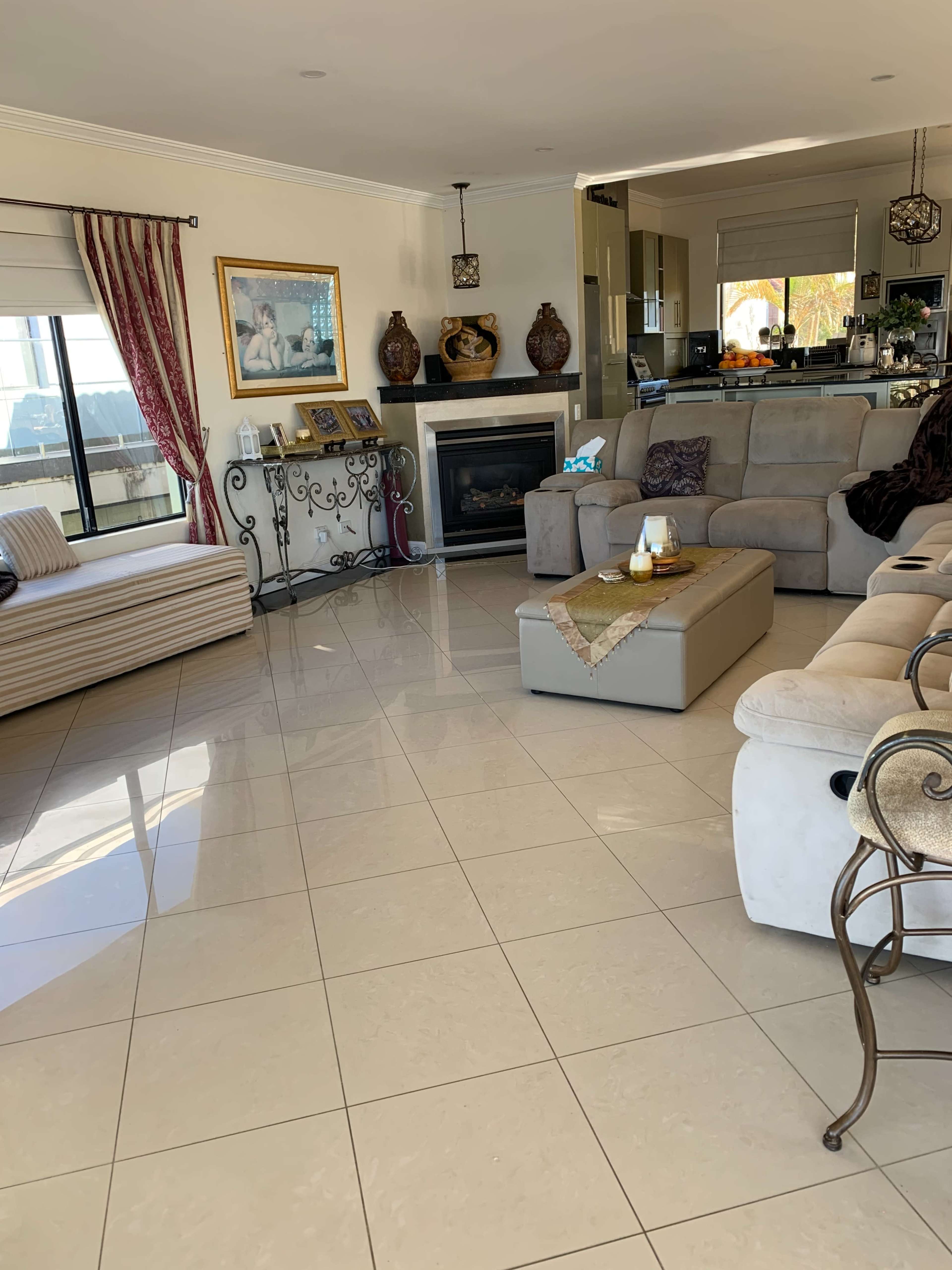A living room with a beige couch, a coffee table, and a fireplace, featuring tiled floors and decorative items on shelves.