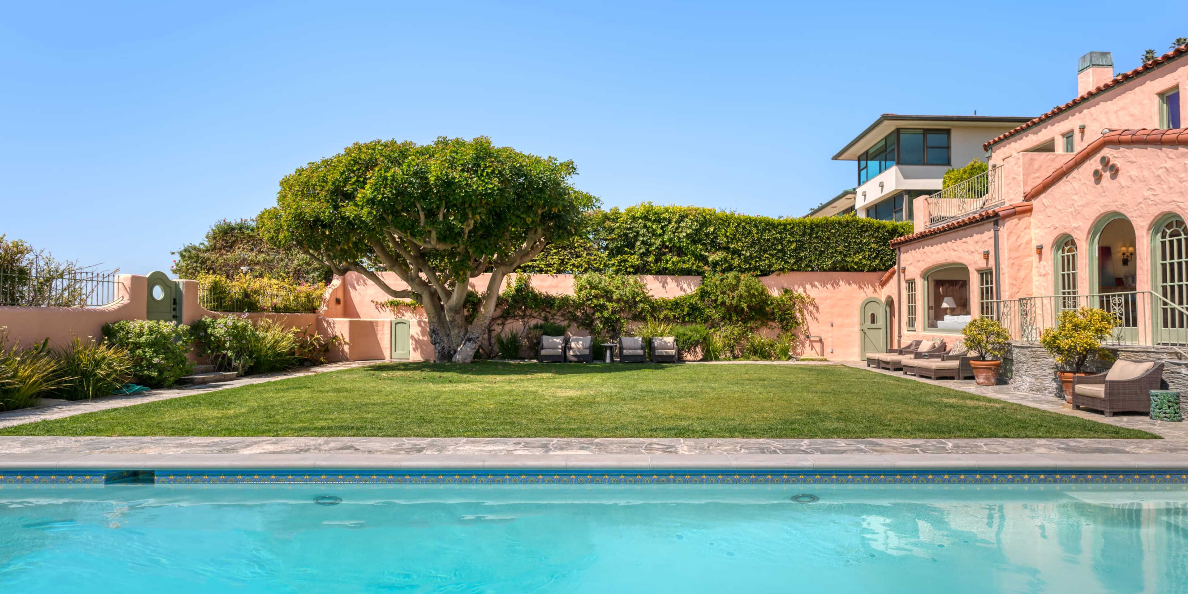 The image shows a landscaped backyard with a swimming pool, a green lawn, a tree, and a seating area beside a house.