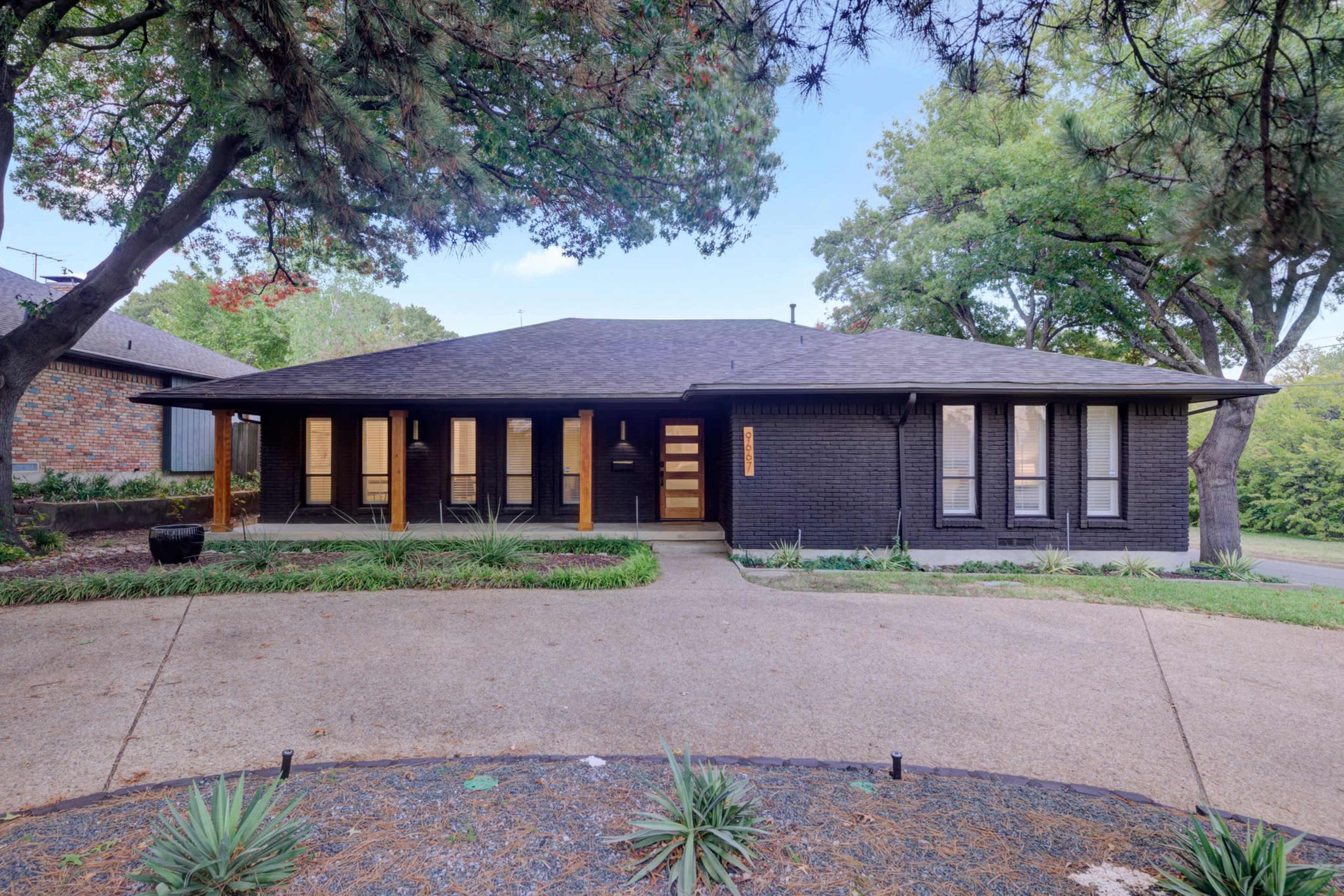 A modern single-story house with a black exterior and a landscaped driveway features multiple large windows and a central entrance.