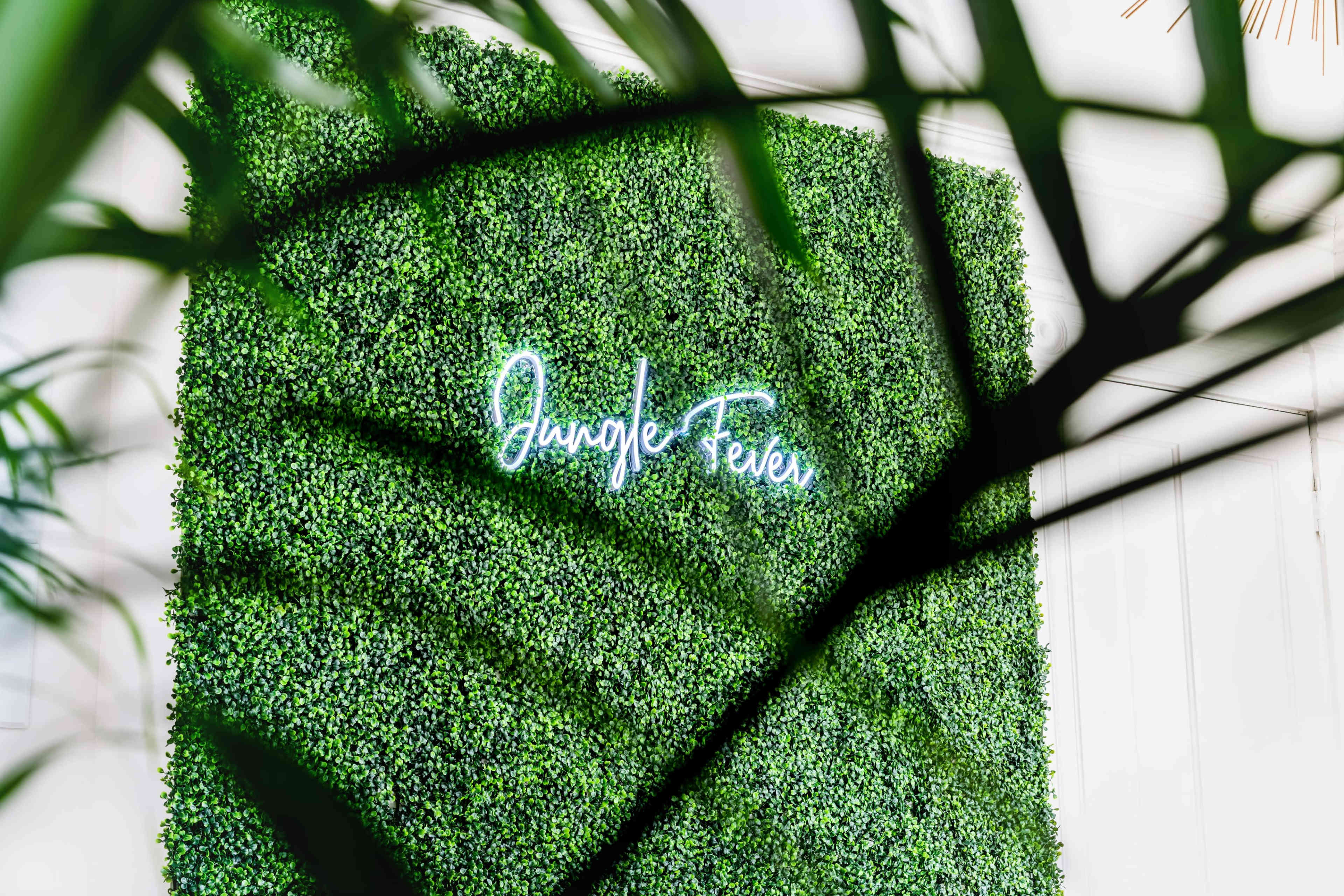 A vibrant green wall covered in artificial foliage features the words "Jungle Fever" in neon lights.