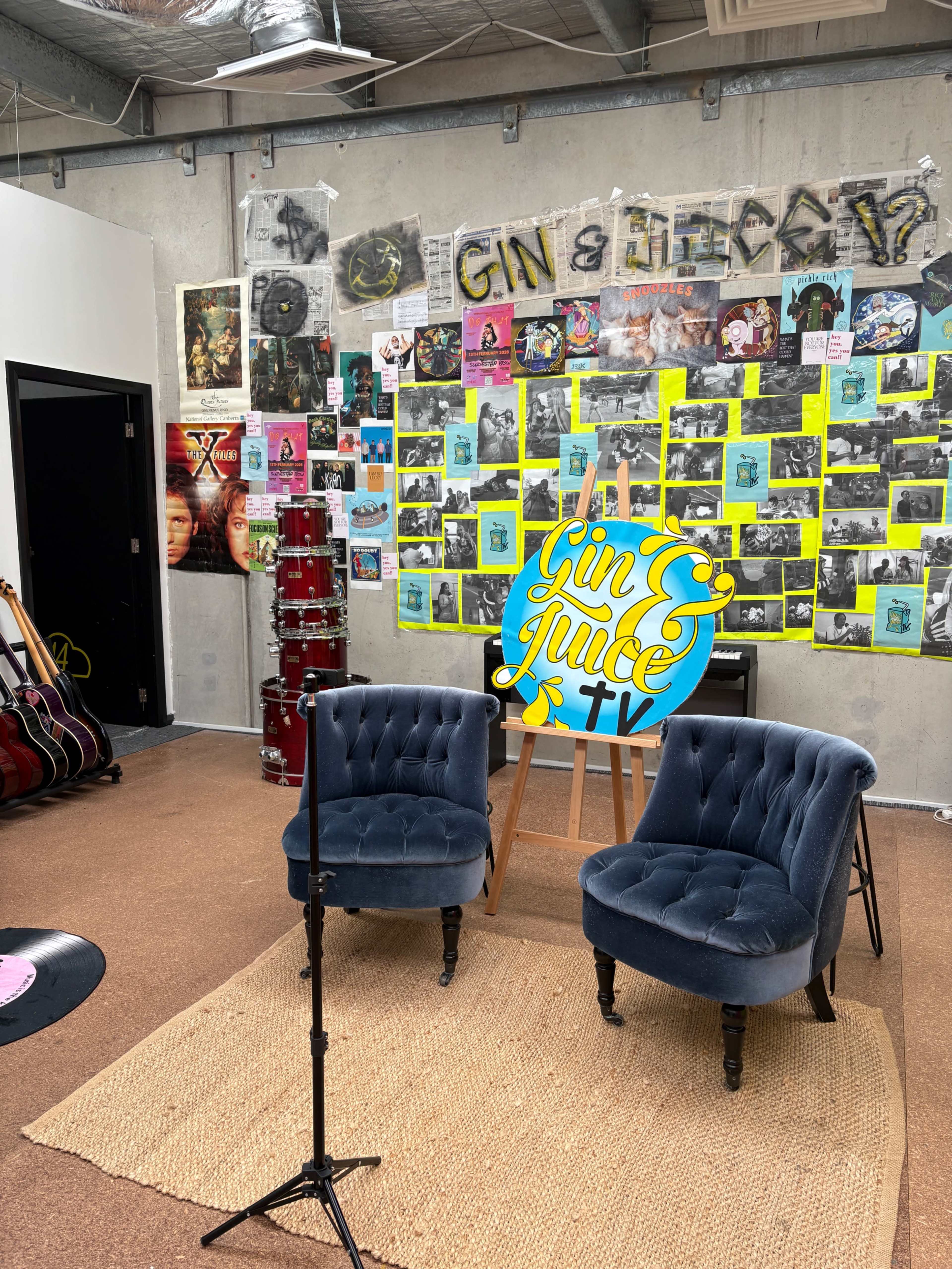The scene features two blue armchairs on a woven rug in front of a vibrant wall covered with colorful posters and a sign that reads "Gin & Juice TV."