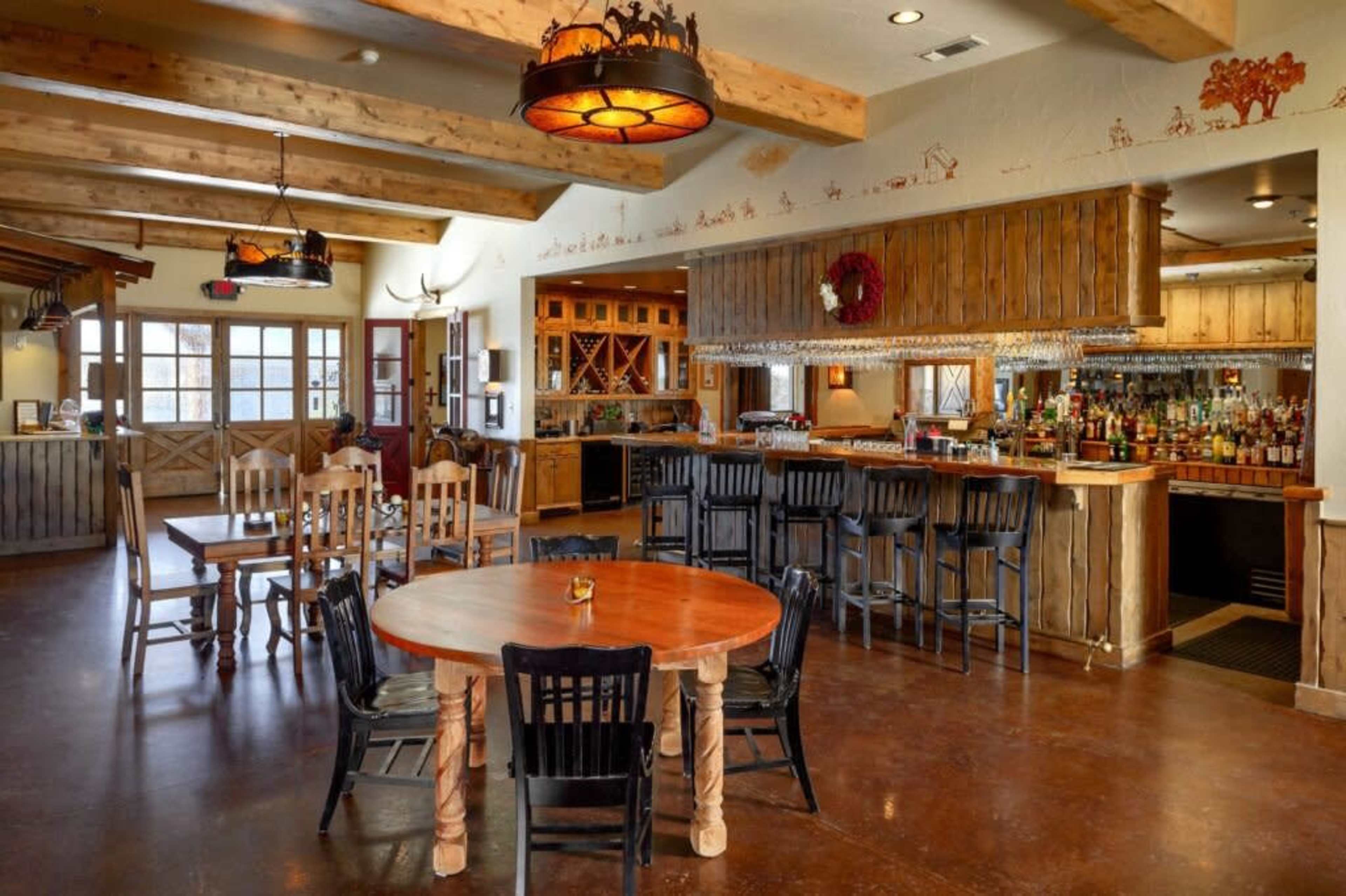 The image shows a spacious interior of a rustic dining area with wooden beams, a bar, and several tables and chairs.