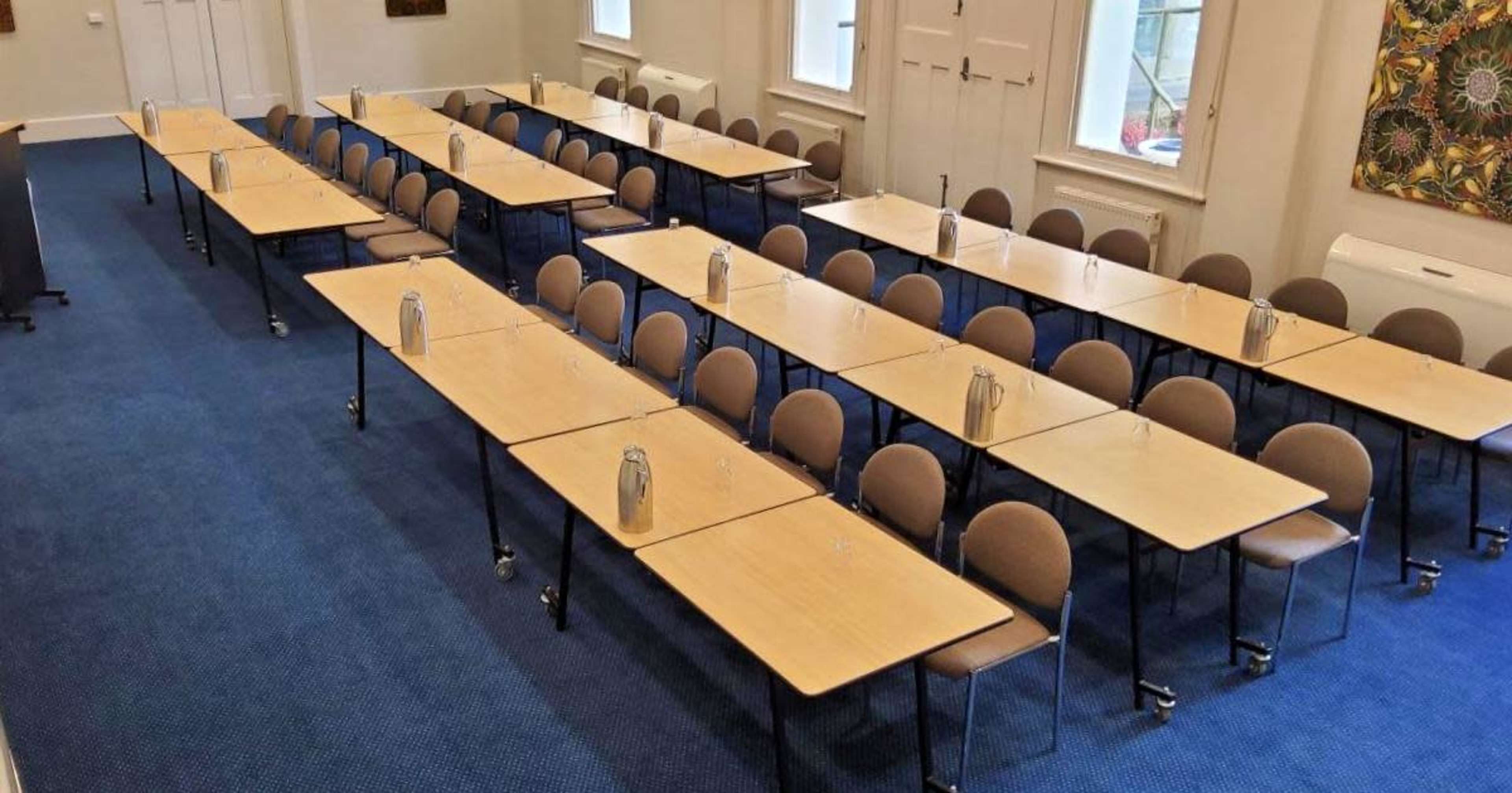 A large meeting room is set up with rows of tables and chairs, each table featuring a water pitcher.