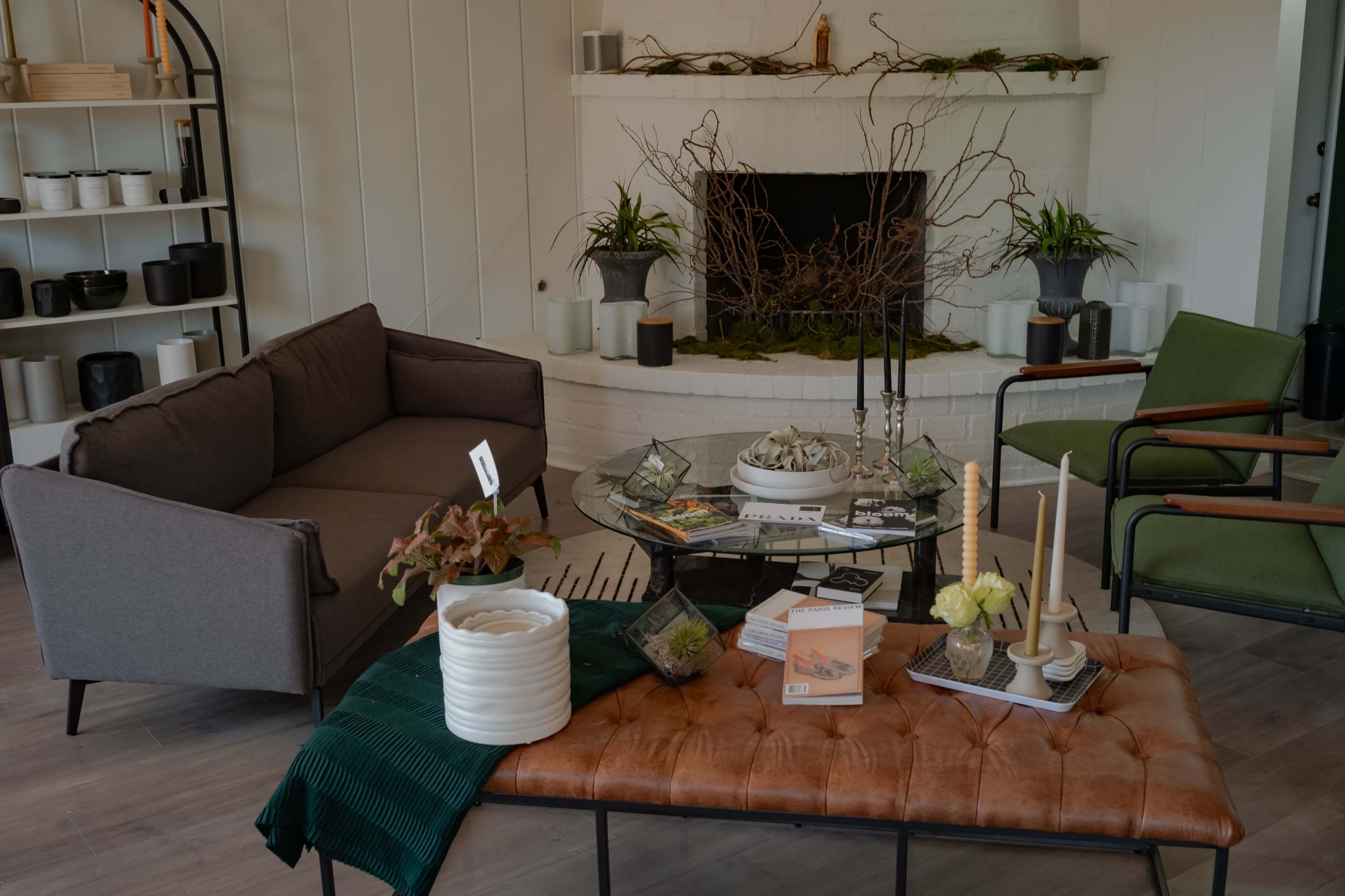 A cozy living room features a gray sofa, two green chairs, a coffee table with decorative items, and a fireplace adorned with plants and branches.