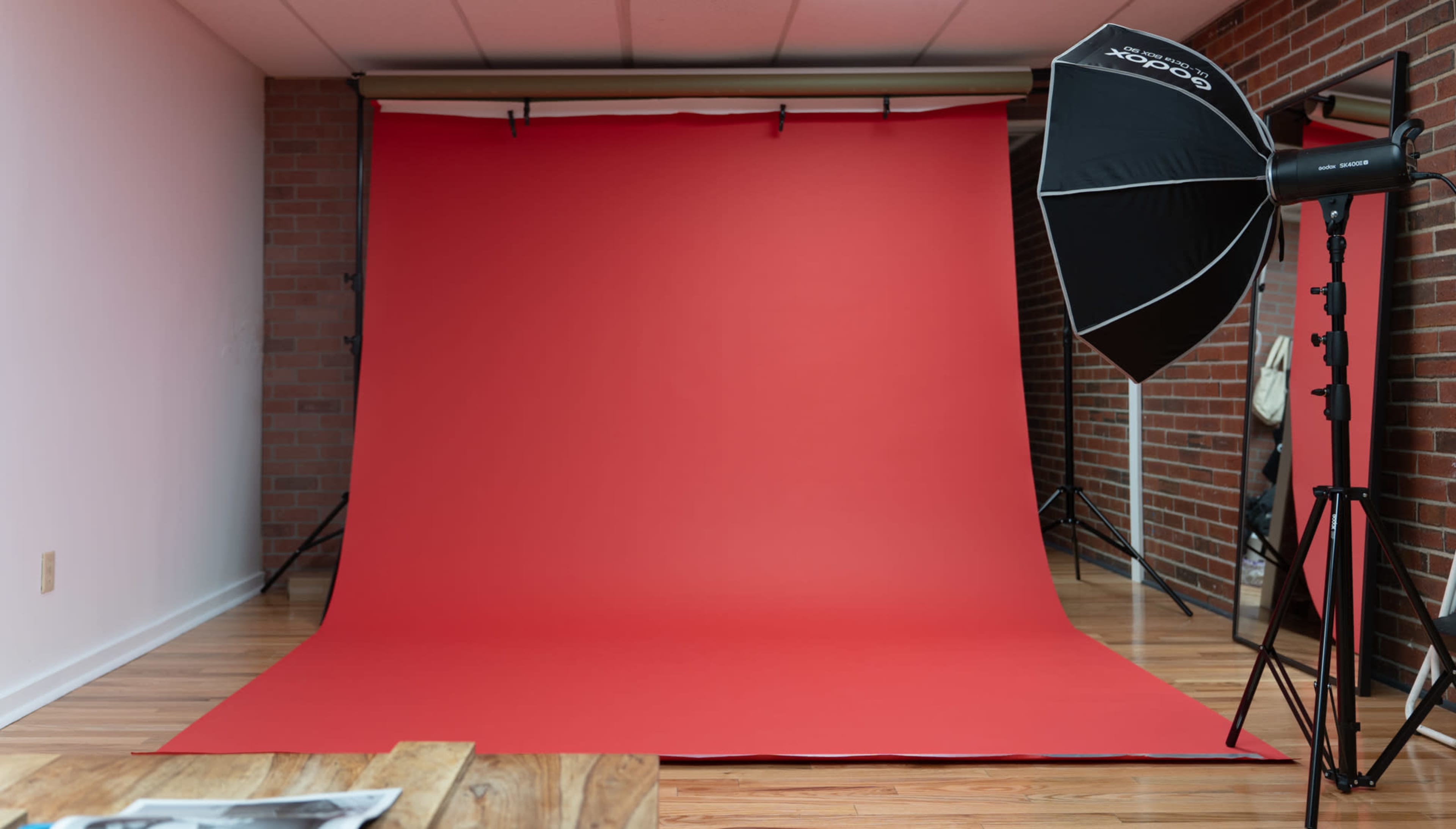 The image shows a photography studio with a vibrant red backdrop and a large softbox light positioned to the side.