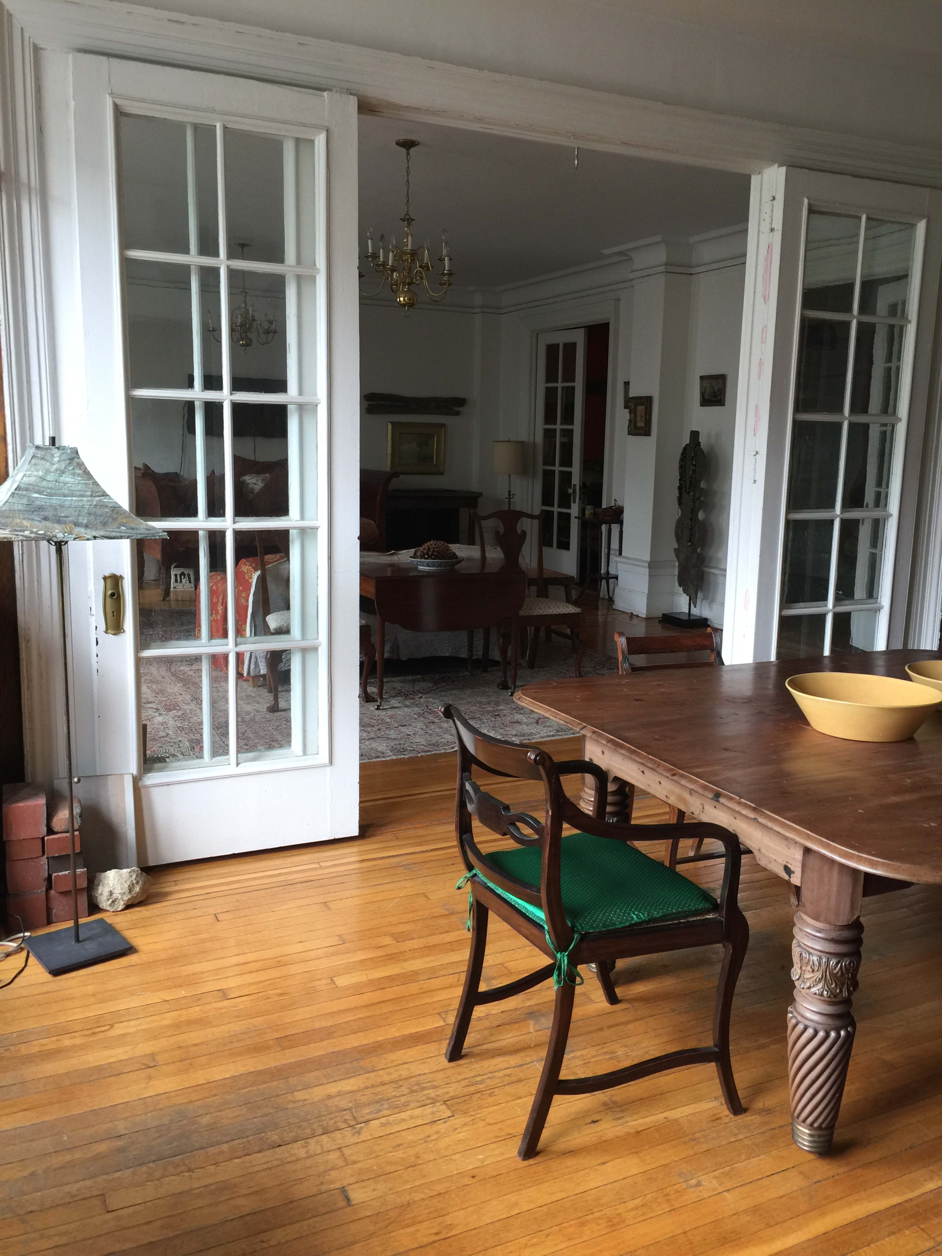 The image shows a dining room with a wooden table and green chair, leading into a living area through glass-paneled doors.