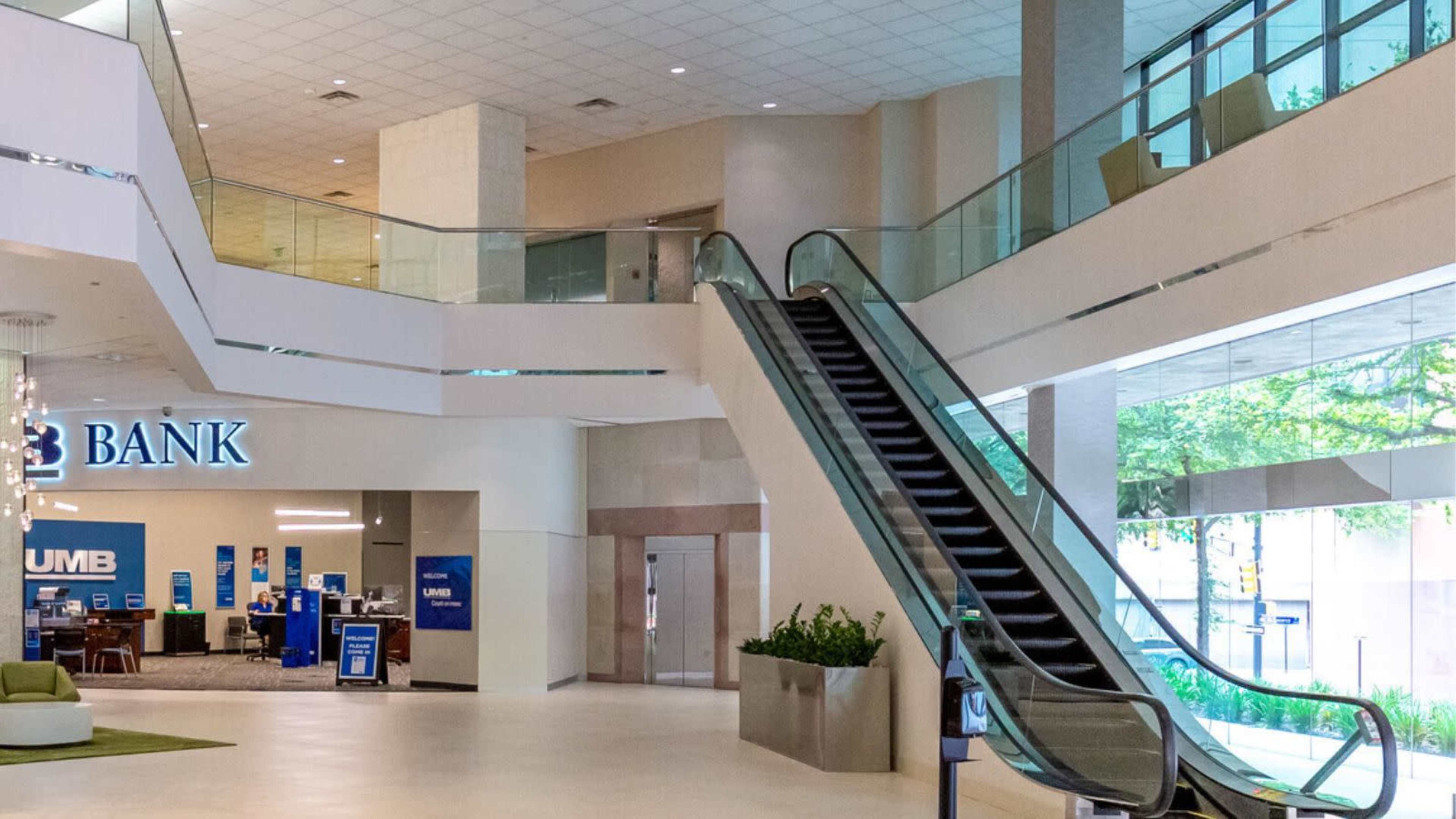 The image shows the interior of a modern bank with an escalator, seating area, and bank signage visible.