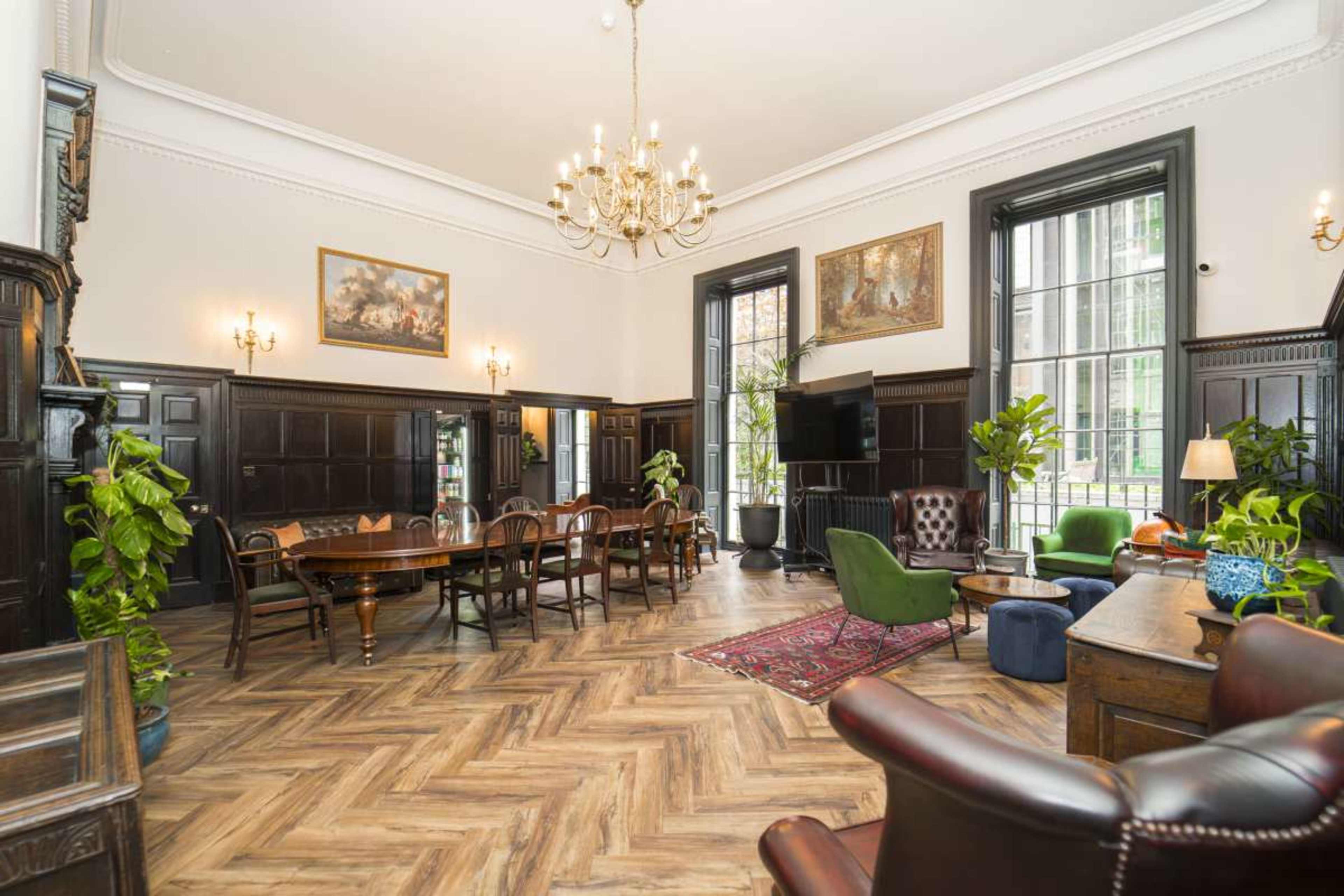The image shows a spacious room featuring a dining table, comfortable seating areas, decorative plants, and large windows, all within an elegantly designed interior.