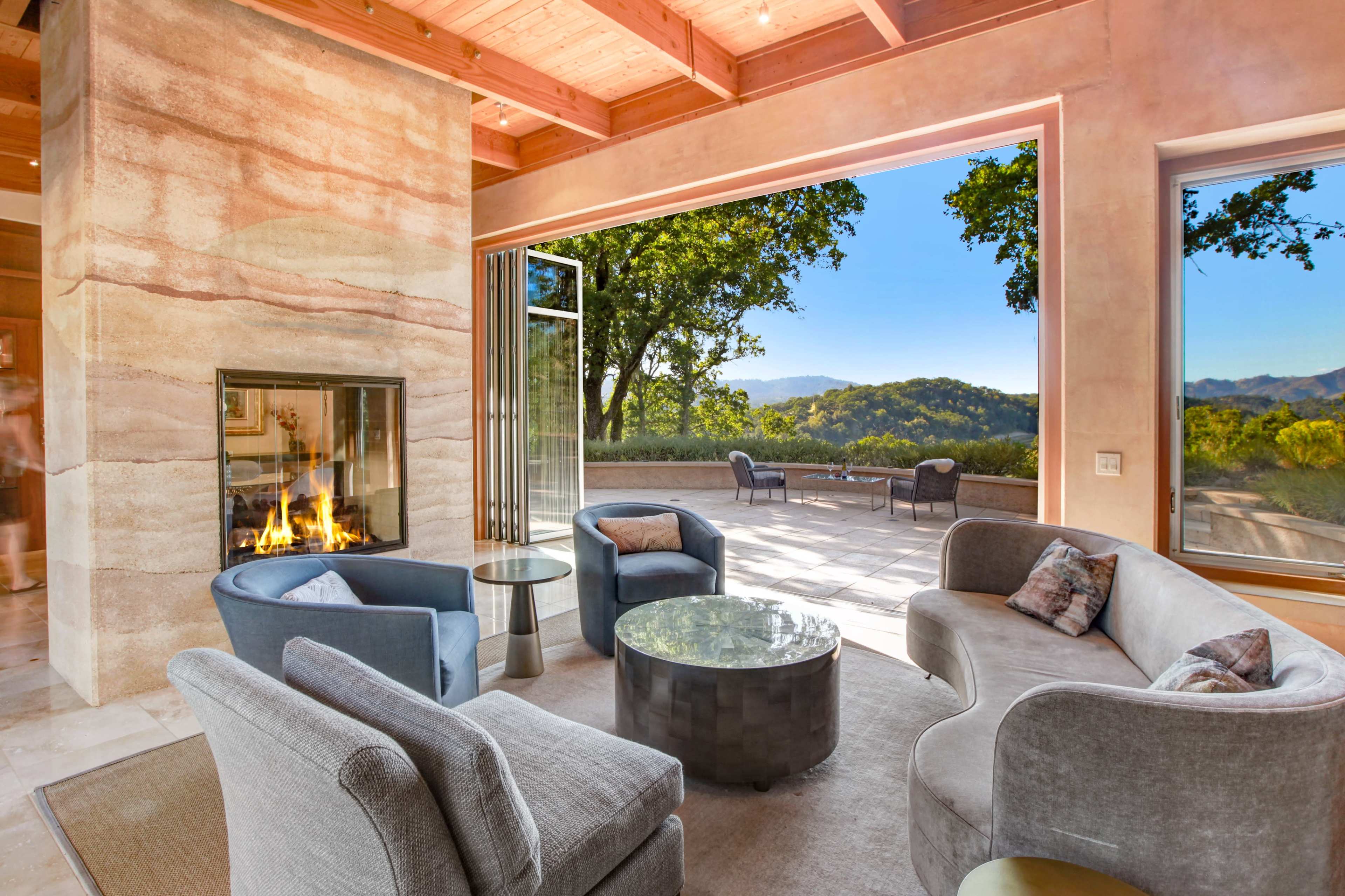 A modern living room with a fireplace, large windows overlooking a scenic view, and contemporary furniture arrangements.