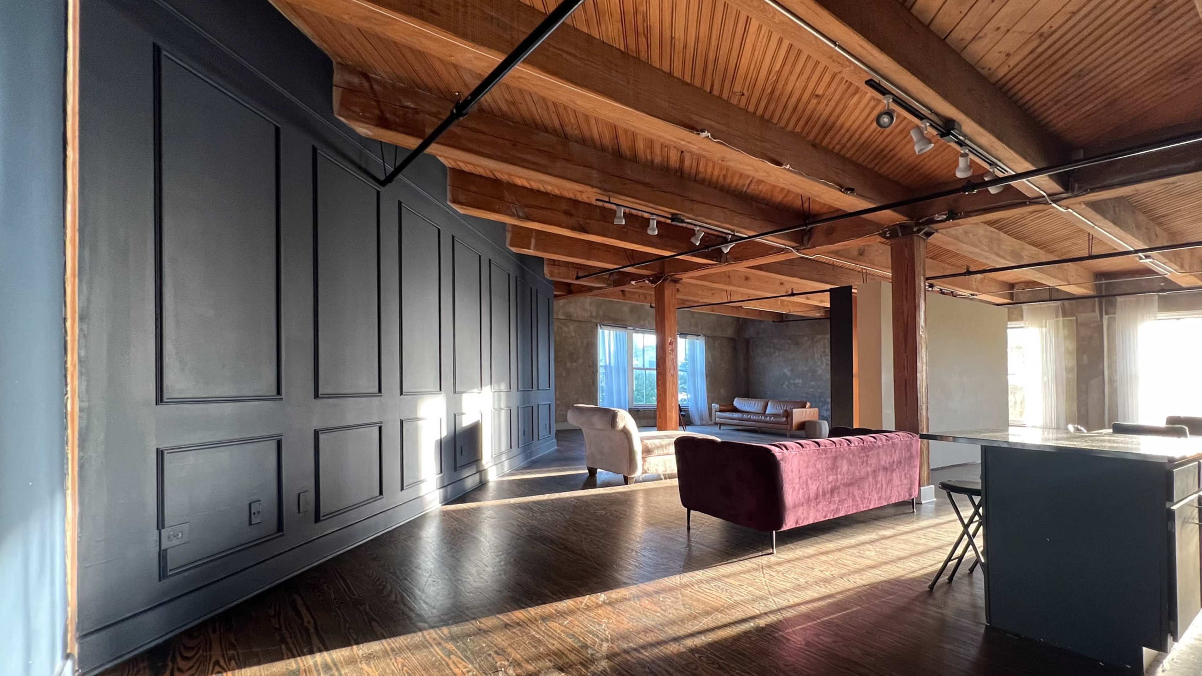 A spacious room with wooden beams, a gray wall, and various seating arrangements, including a purple couch and chairs.