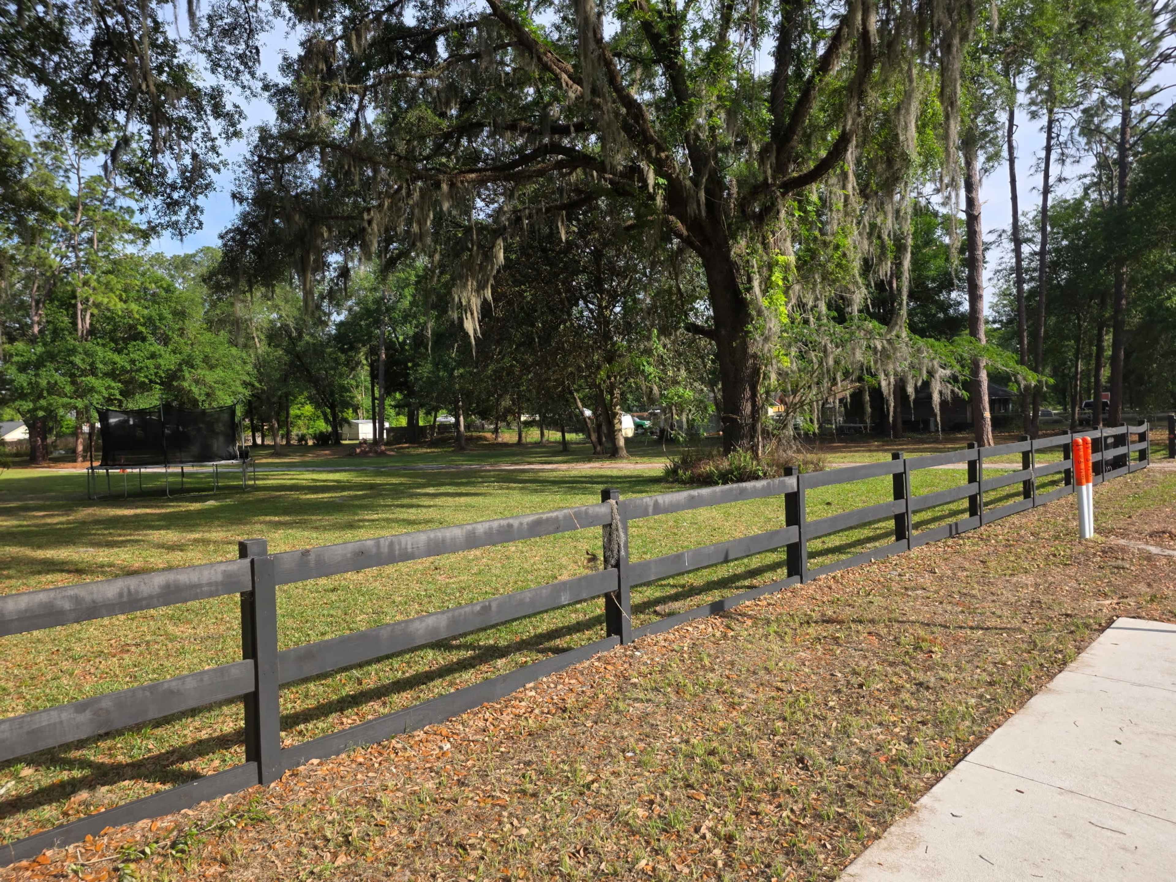 A black wooden fence runs alongside a grassy area with trees and a trampoline in the background.