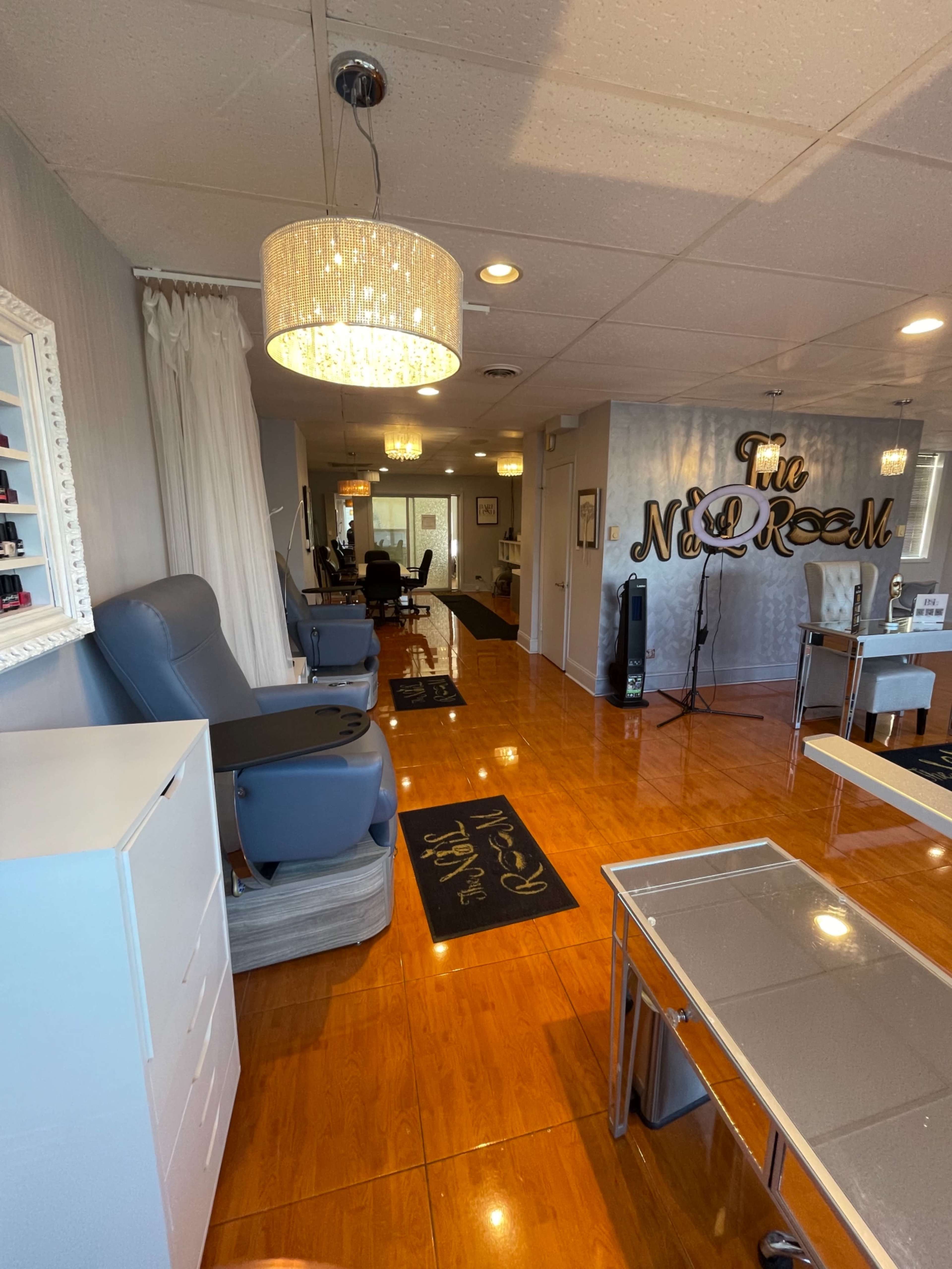 The image shows the interior of a nail salon with polished wooden floors, manicure stations, and plush seating arranged neatly under decorative lighting.