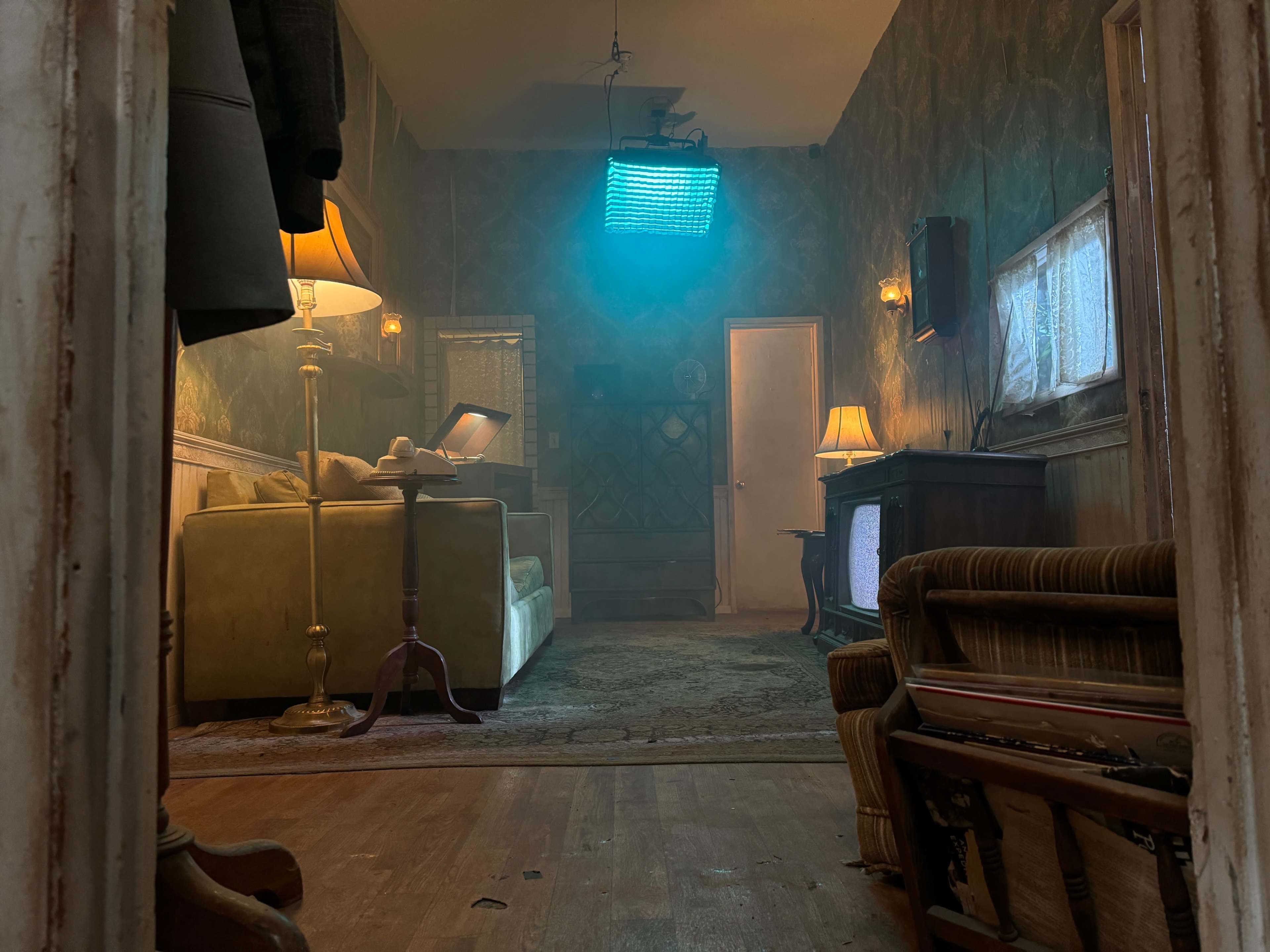 A dimly lit, vintage-style room featuring a couch, wooden furniture, and a glowing light source in the ceiling.