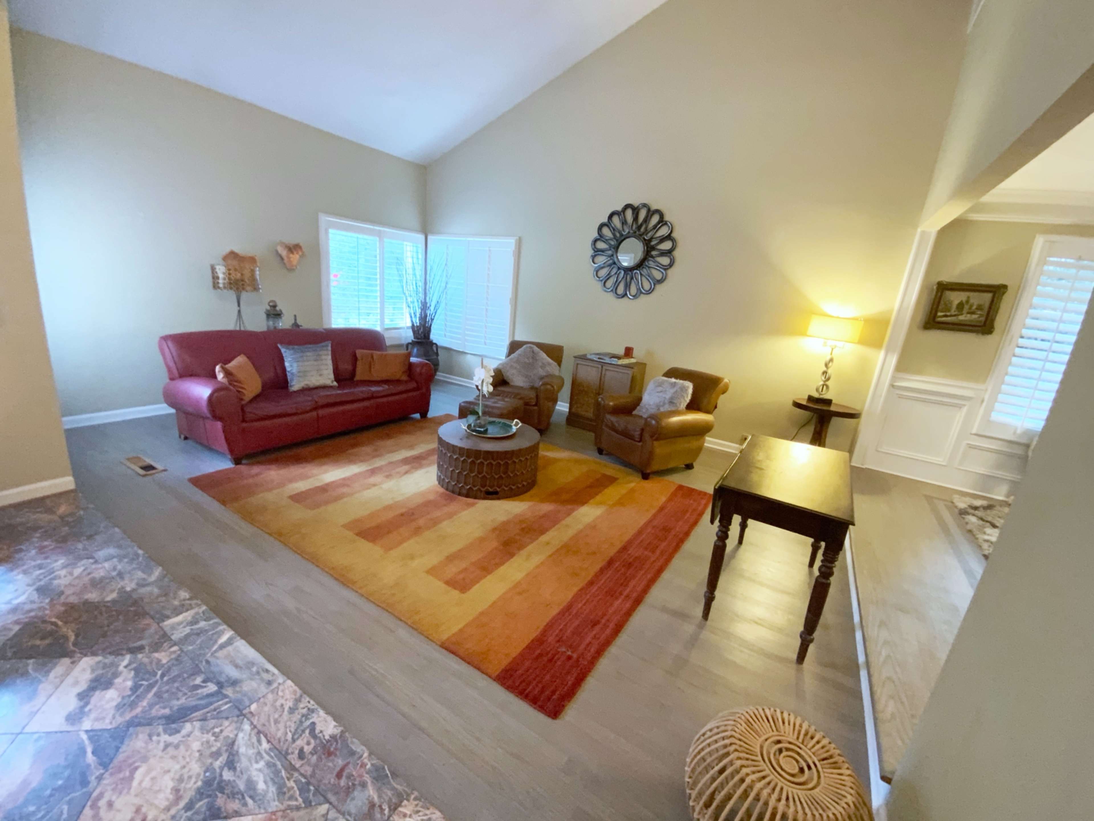 A living room featuring a red sofa, two armchairs, a coffee table on a patterned area rug, and a lamp beside a side table.