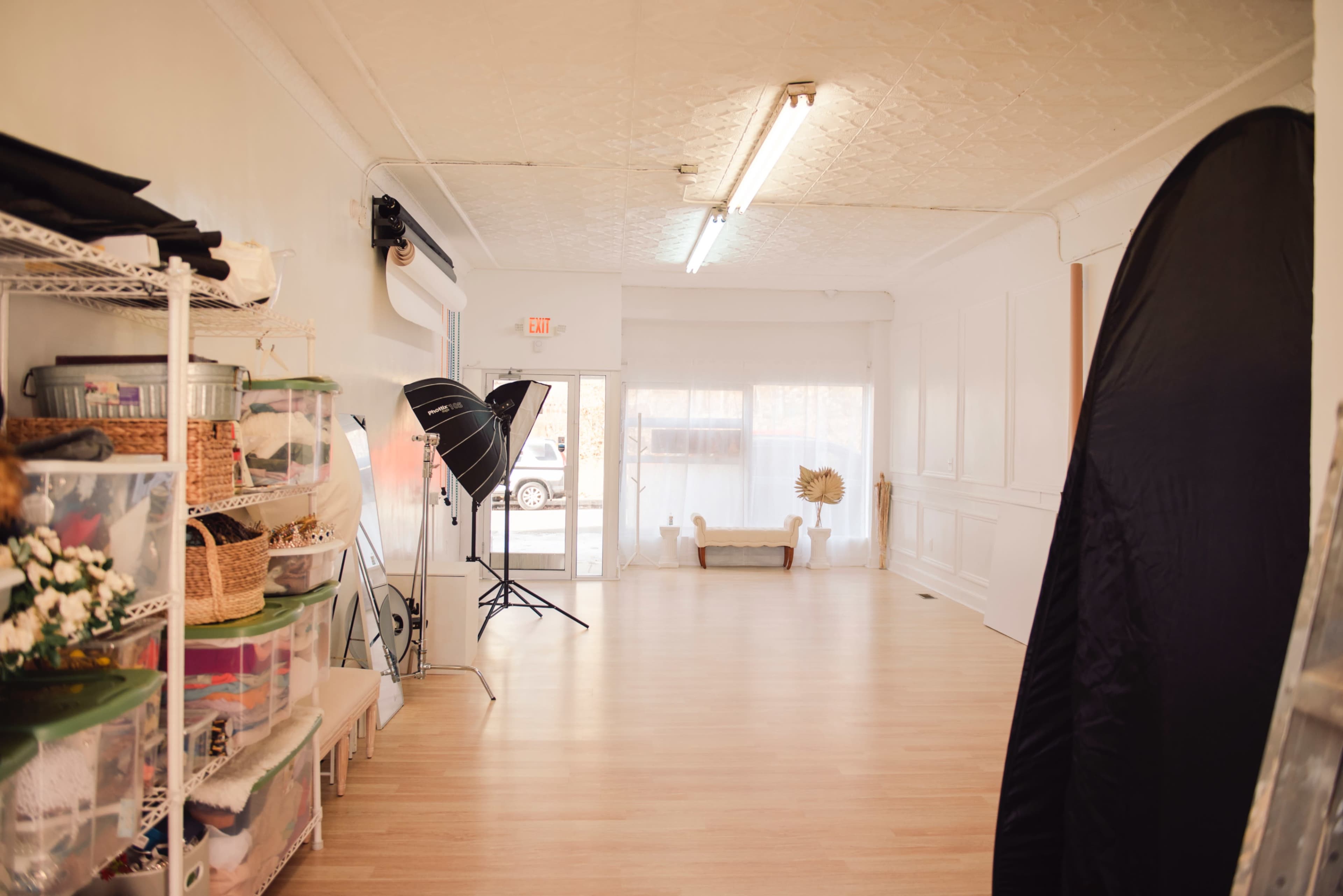 An empty photography studio with soft lighting, storage bins, and large backdrop stands.