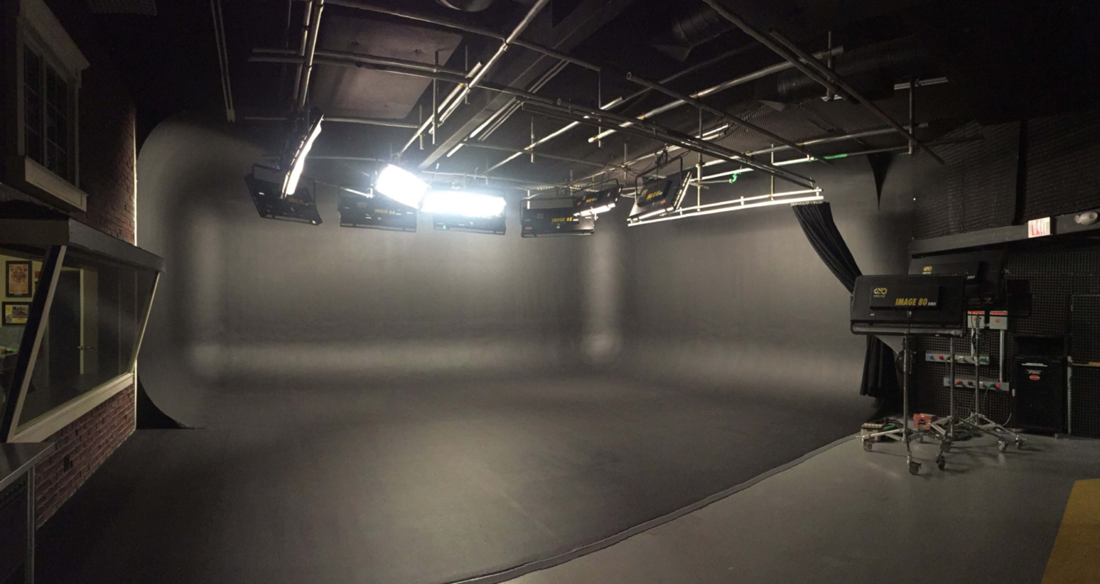 The image shows an empty studio with a black backdrop, overhead lights, and studio equipment on the side.