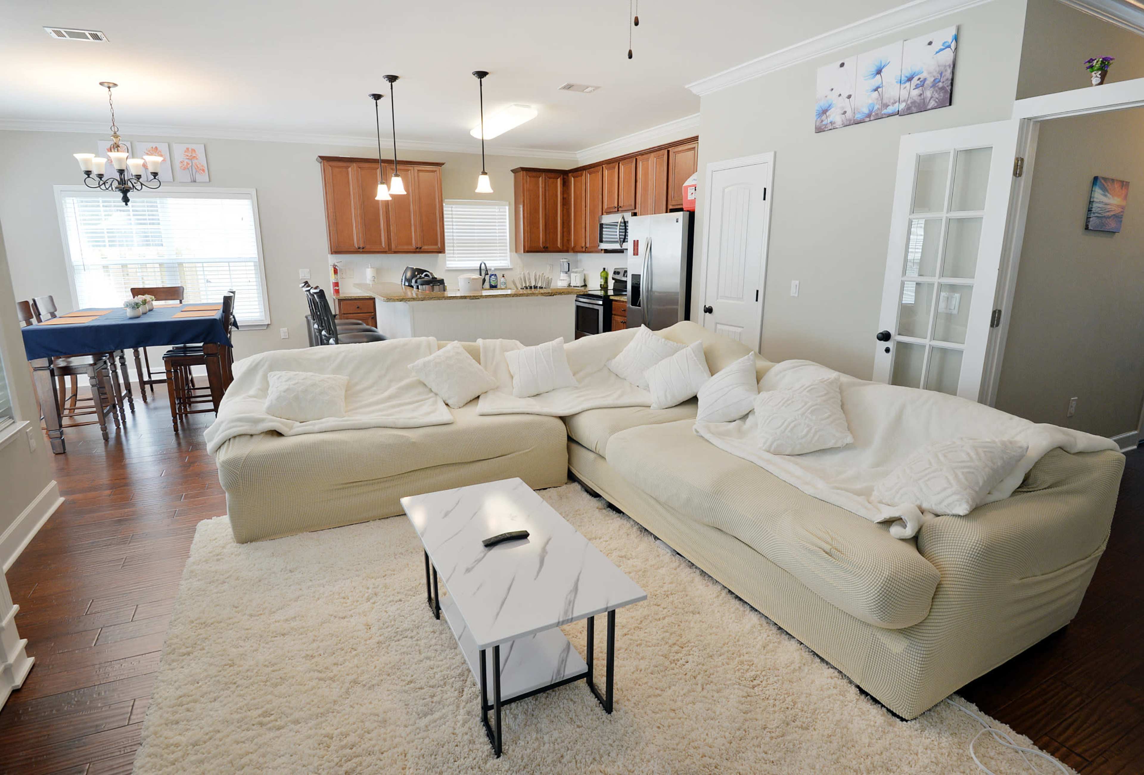 A living room with a large sectional sofa, a coffee table, and an open kitchen in the background.