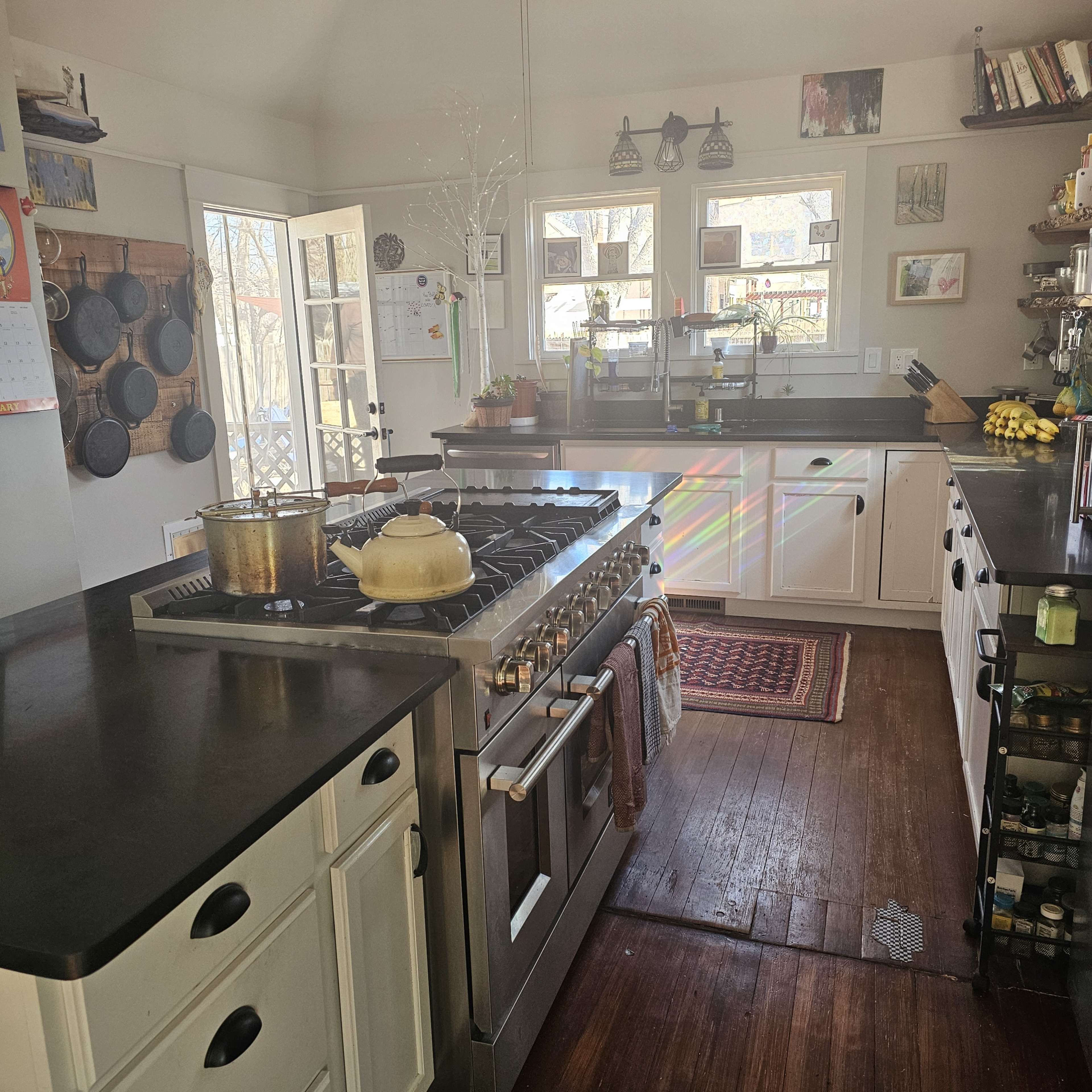 The kitchen features a gas stove with a pot on it, white cabinetry, a wooden floor, and a window allowing natural light to enter.