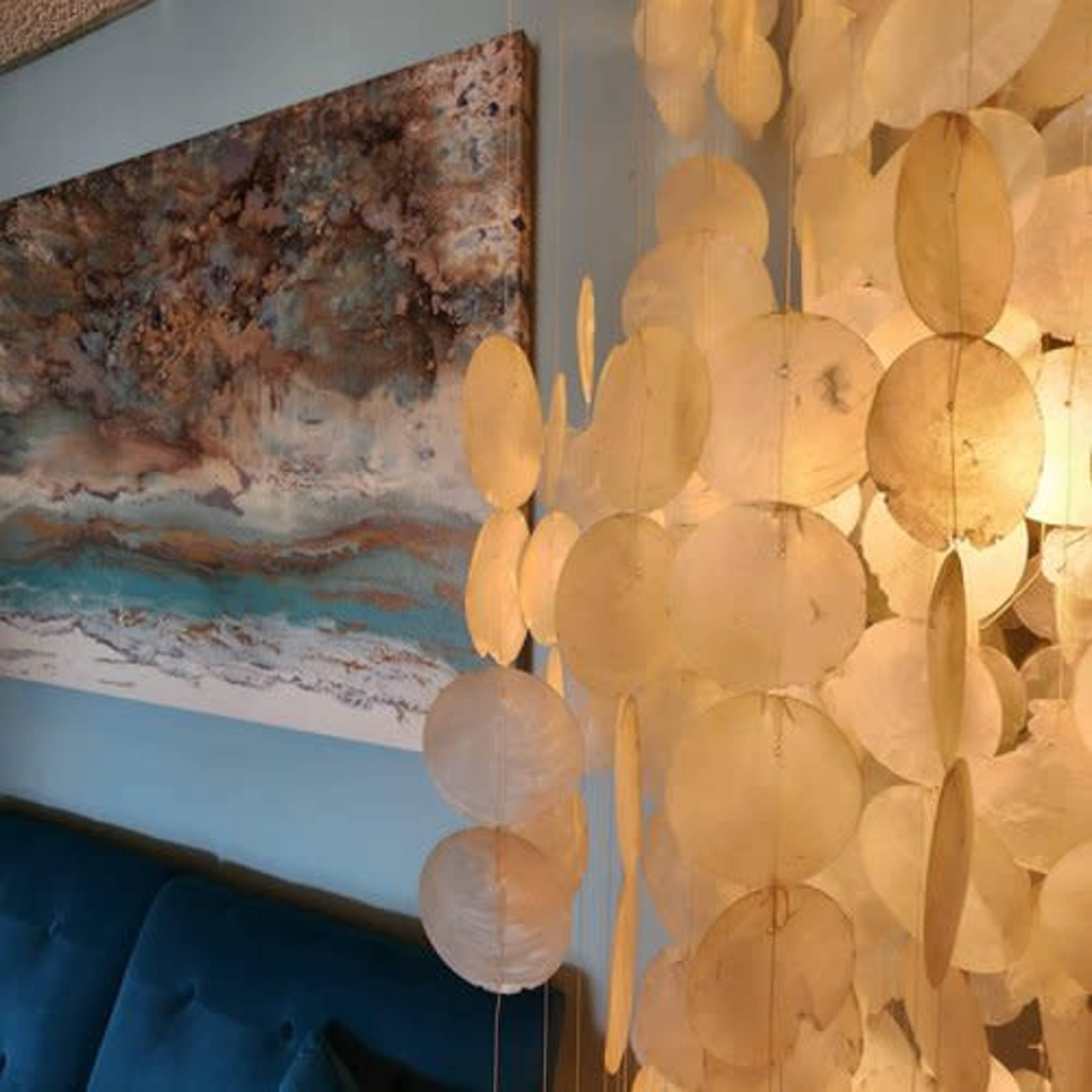 A modern interior decor with a wall art piece above a blue couch and a translucent circular pendant decoration.