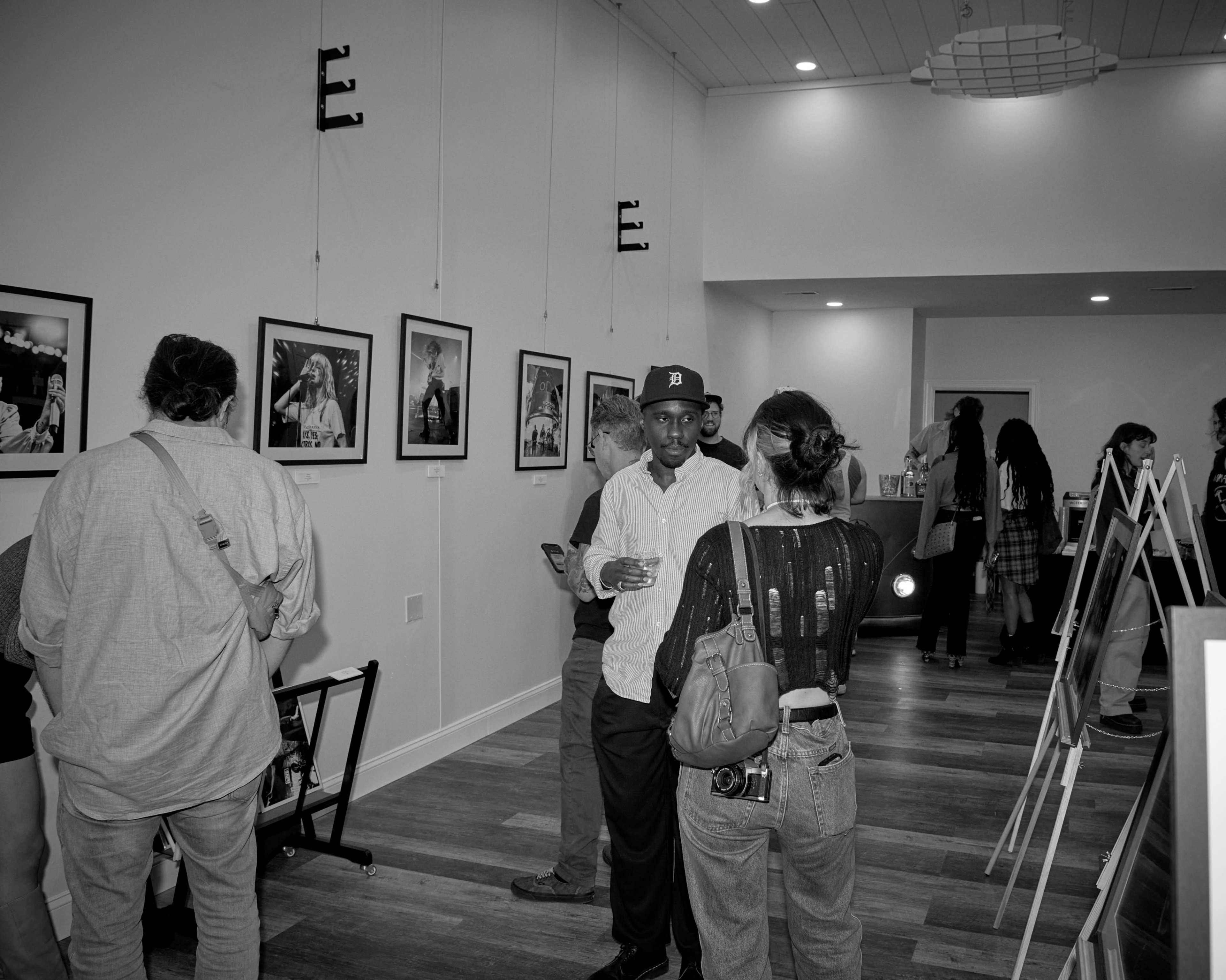 A group of people is gathered in an art gallery, interacting and observing black-and-white photographs displayed on the walls.