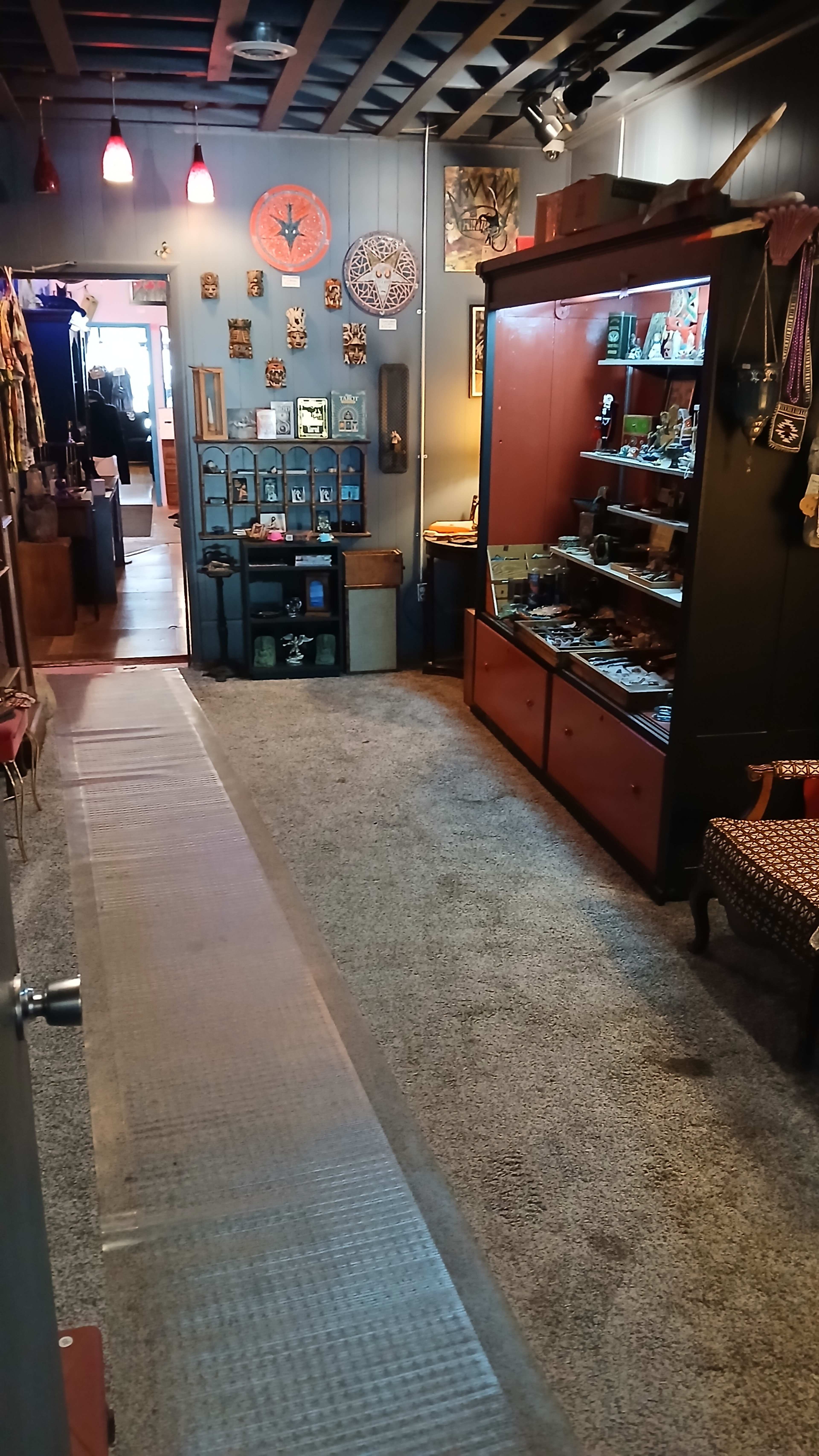 The image shows a narrow hallway leading into a room filled with shelves displaying various collectibles and artifacts, with a carpeted floor and decorative items visible.