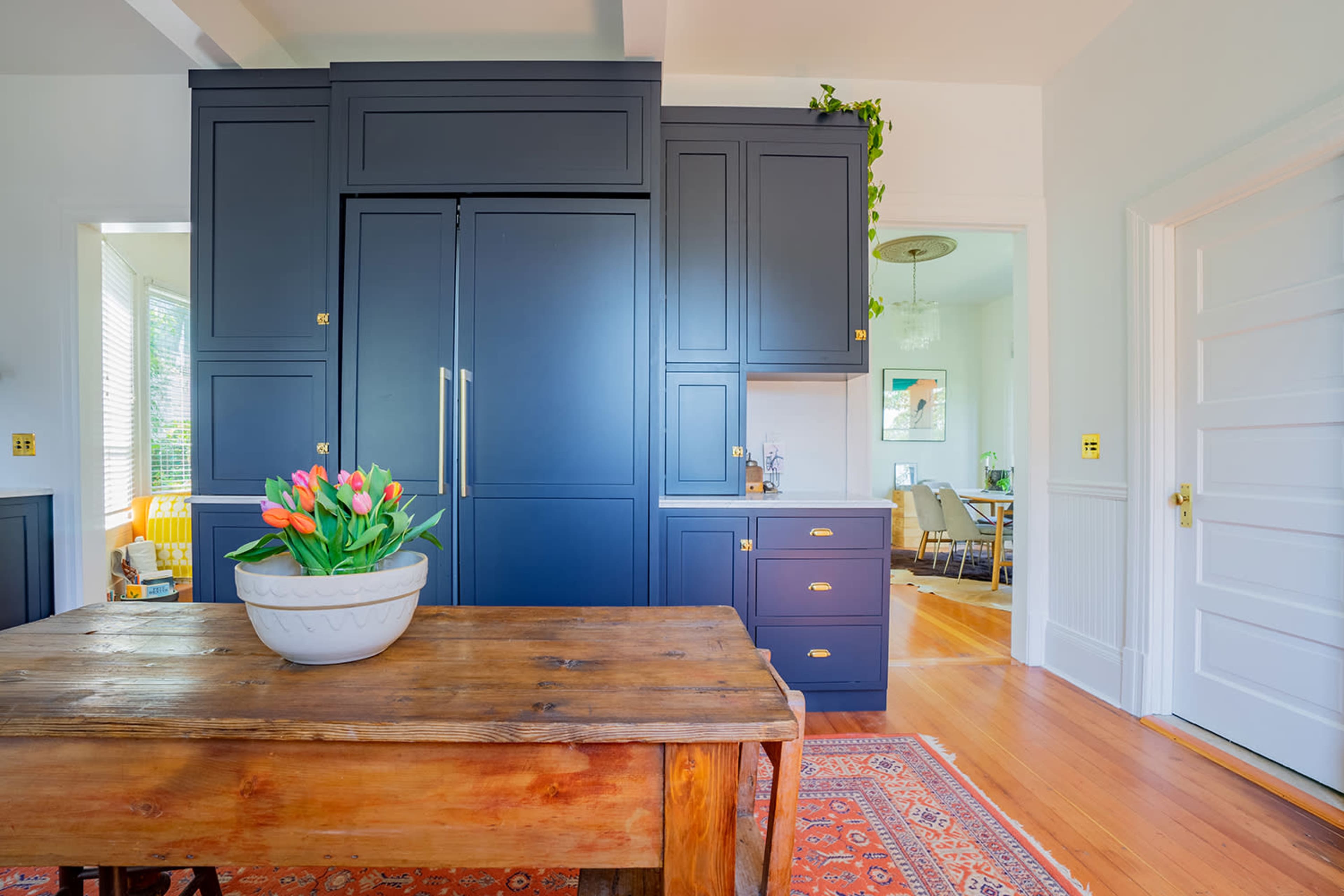 A modern kitchen with navy blue cabinetry, a wooden dining table, and a vase of tulips in the center.