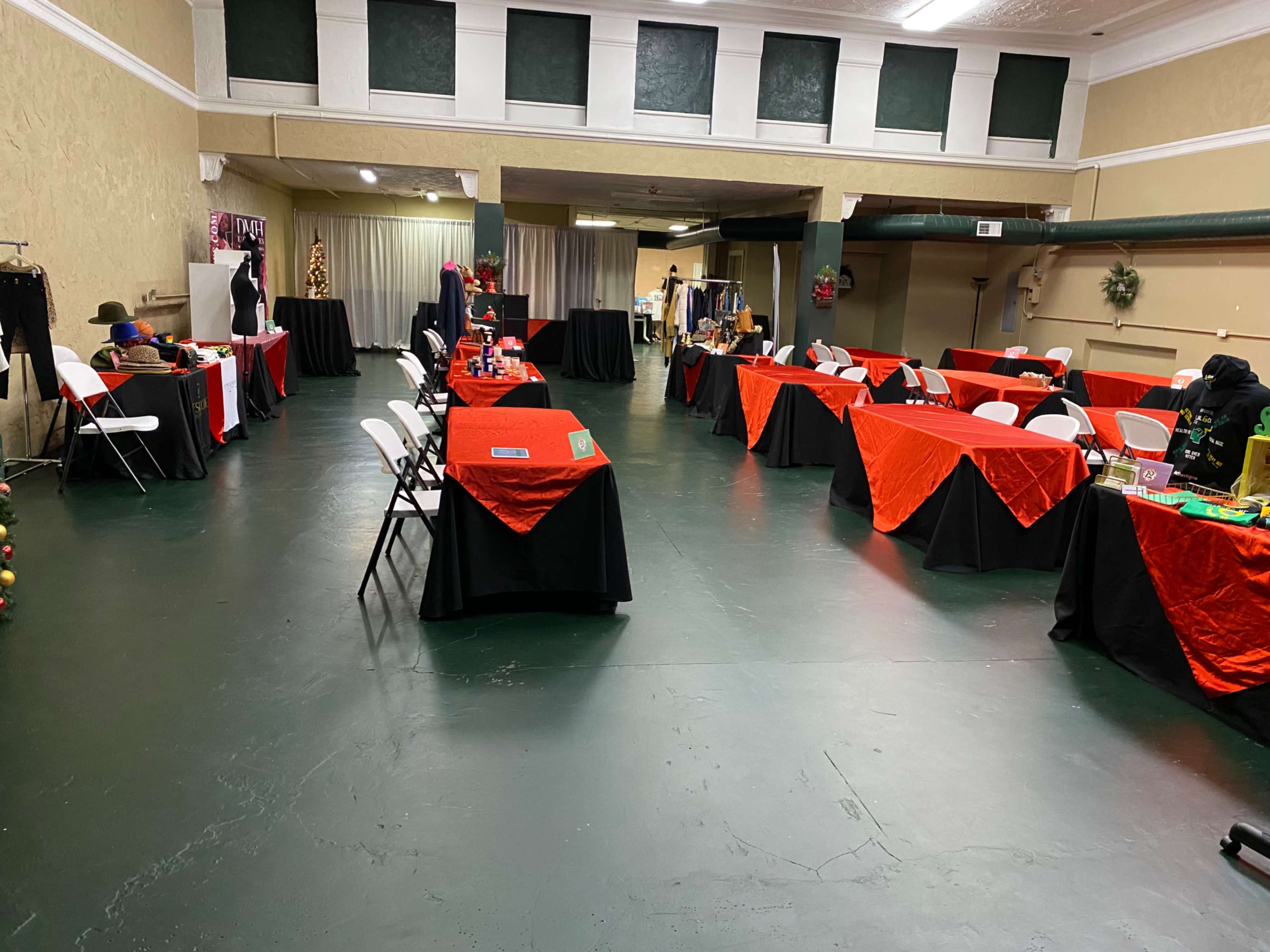A spacious indoor area with several tables covered in red tablecloths and surrounded by chairs, set up for an event or gathering.