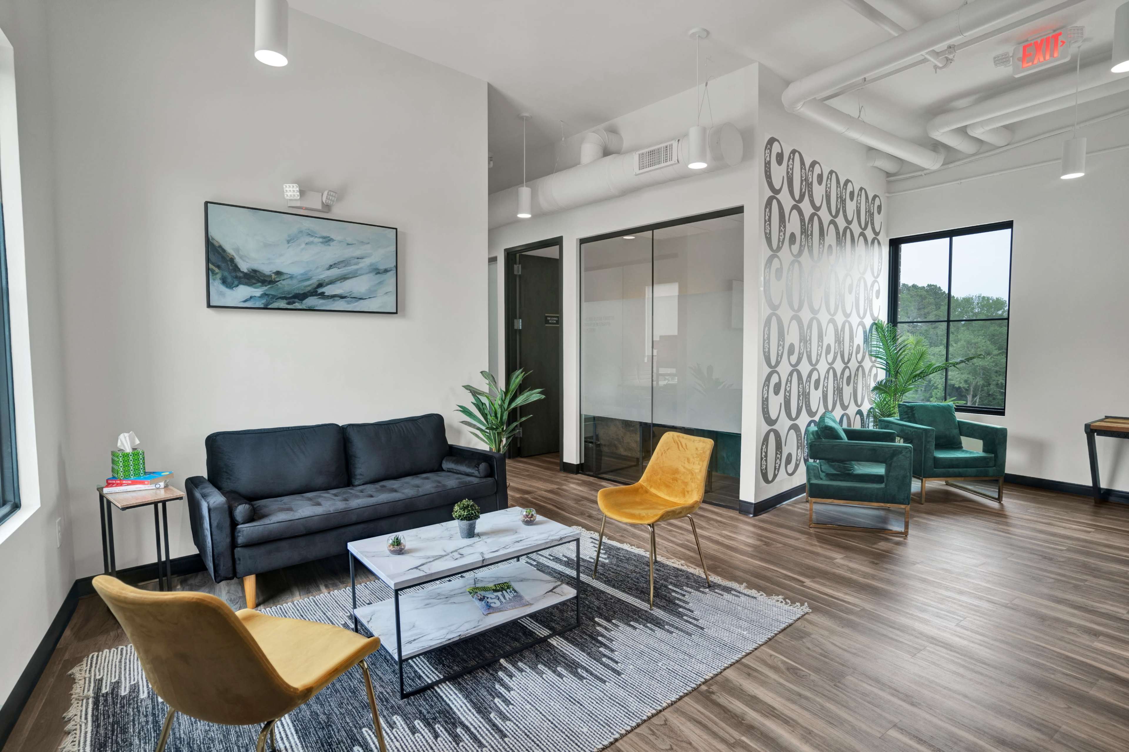 A modern office waiting area features a black sofa, yellow chairs, a marble coffee table, and large windows.
