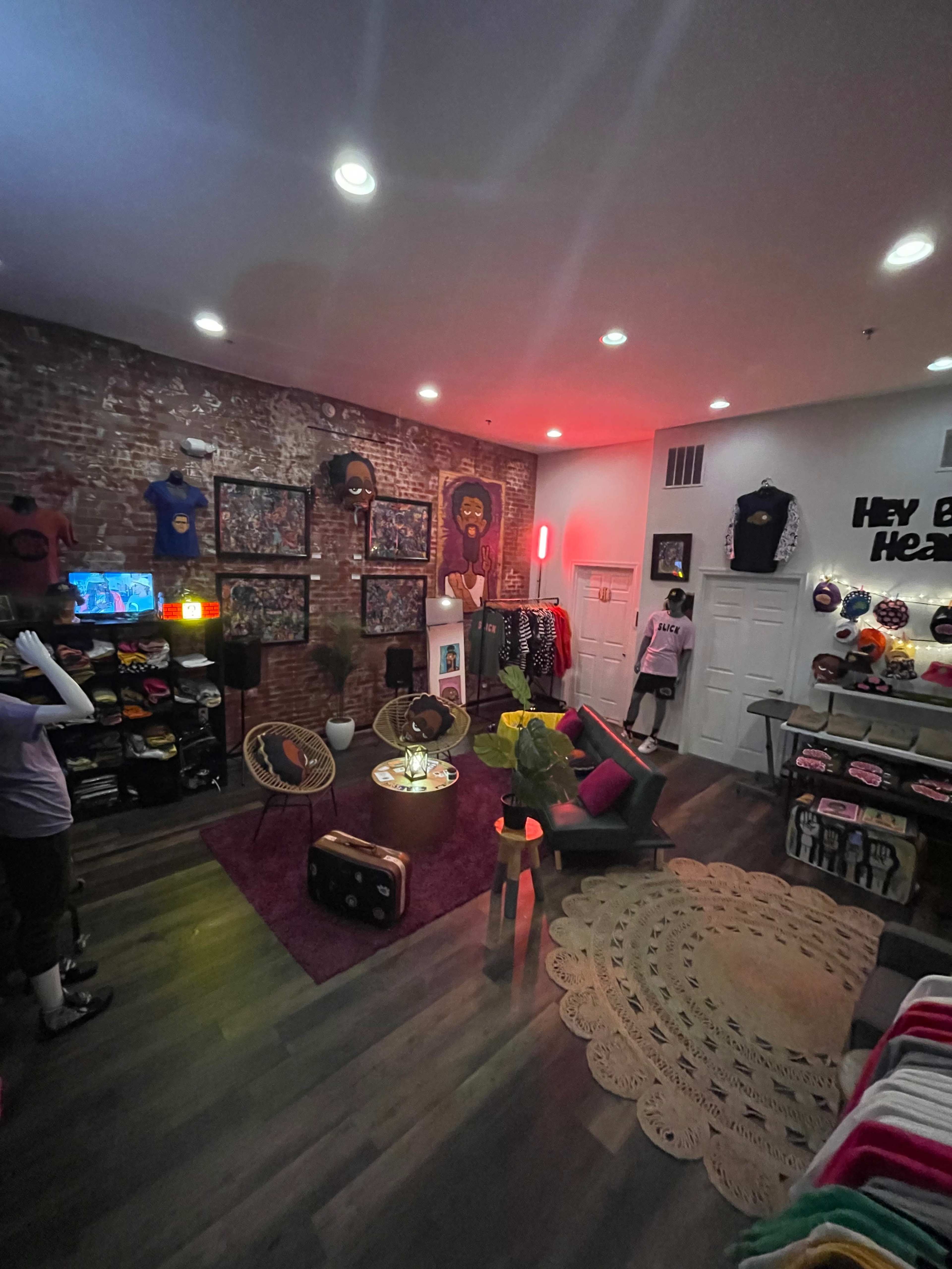 A retail store featuring a variety of T-shirts displayed on racks and walls, with a cozy seating area and colorful lighting.