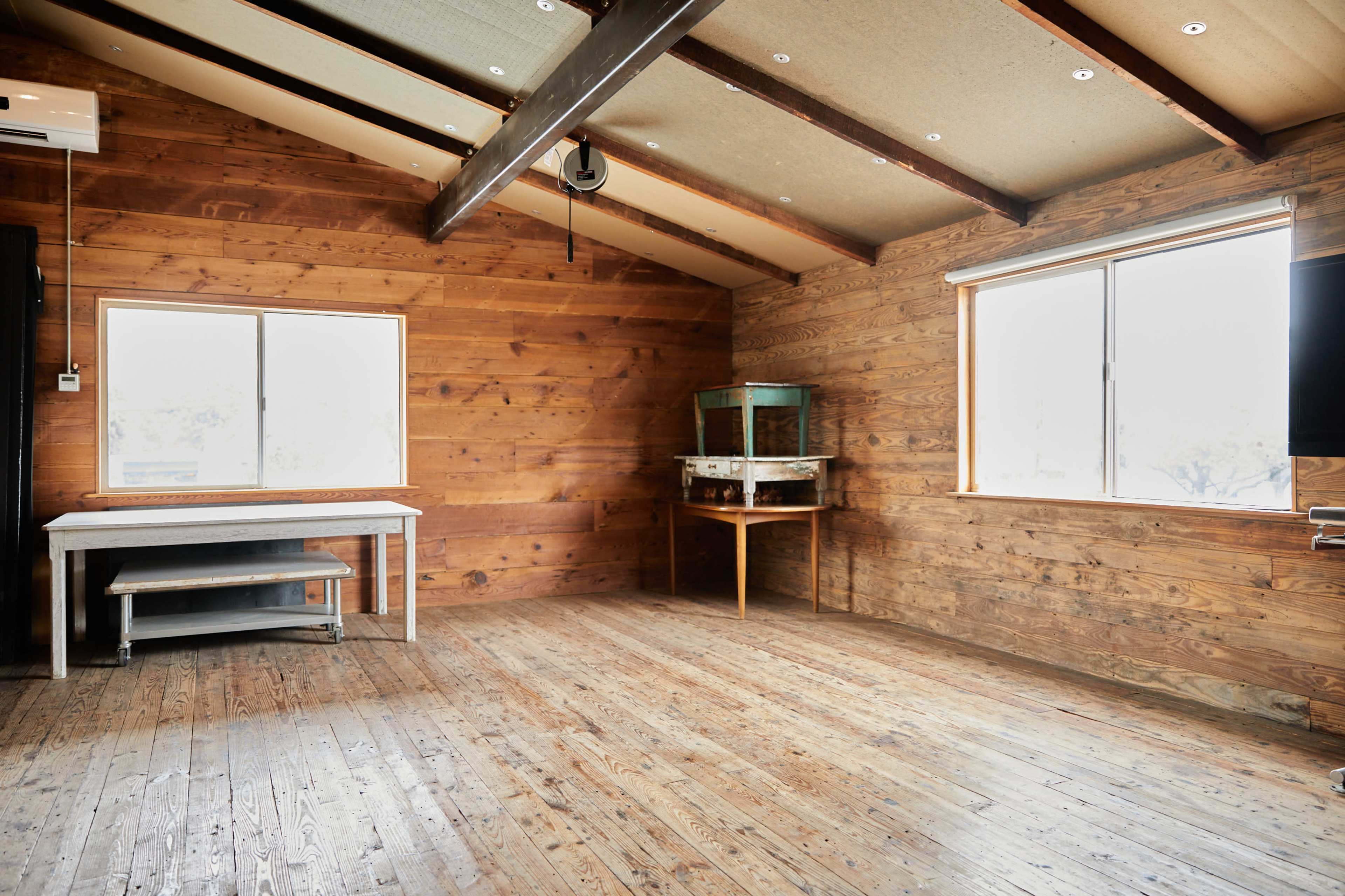 An empty room with wooden walls, a wooden floor, and large windows.