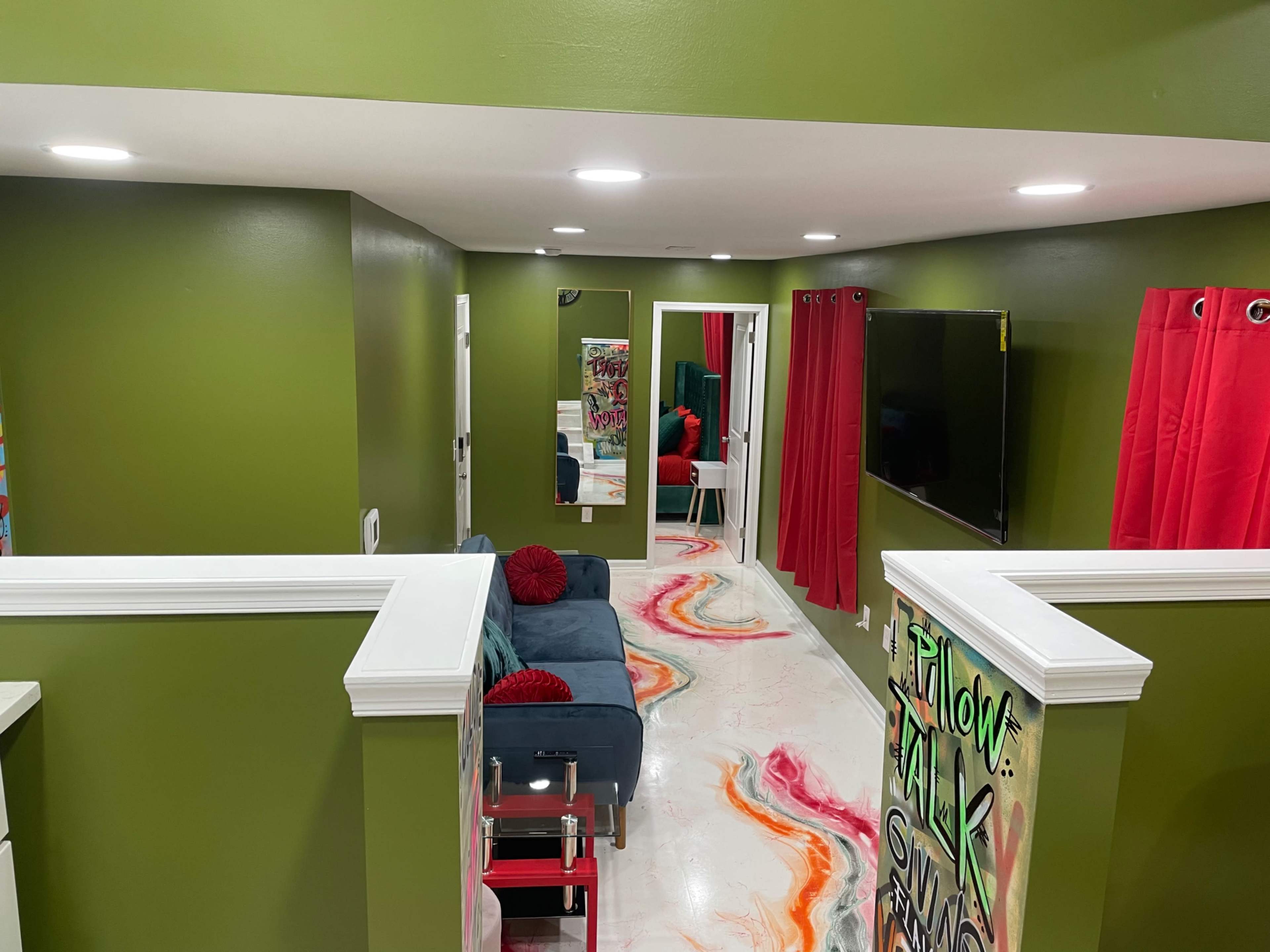 A room with green walls, a teal couch, red curtains, and a colorful, abstract design on the floor.
