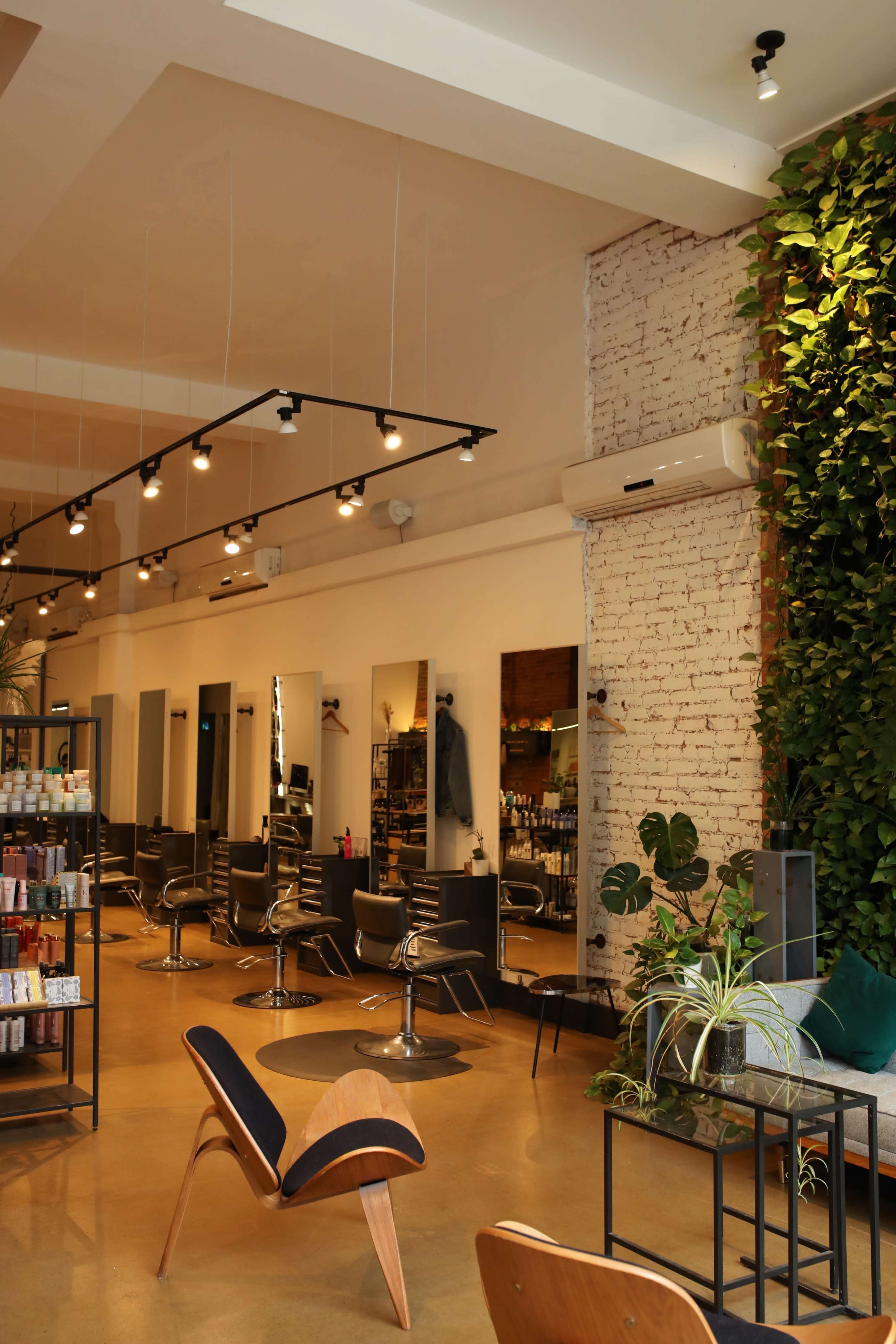 A modern hair salon interior with styling chairs, large mirrors, and a wall covered in greenery.