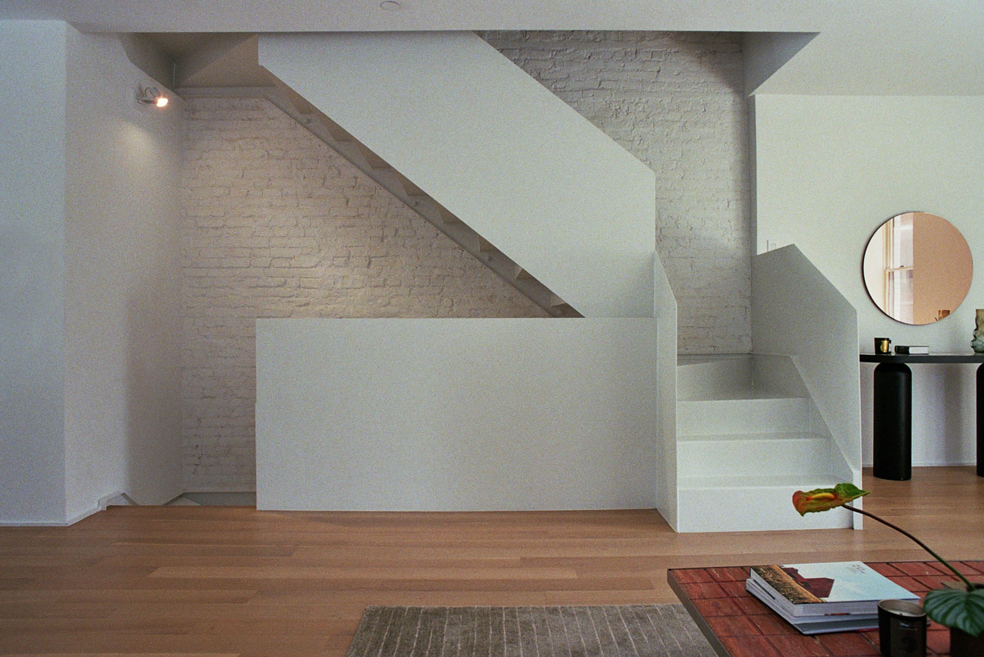 The image shows a modern interior space featuring a staircase with white walls and wooden flooring, complemented by a decorative mirror and minimalist furniture.