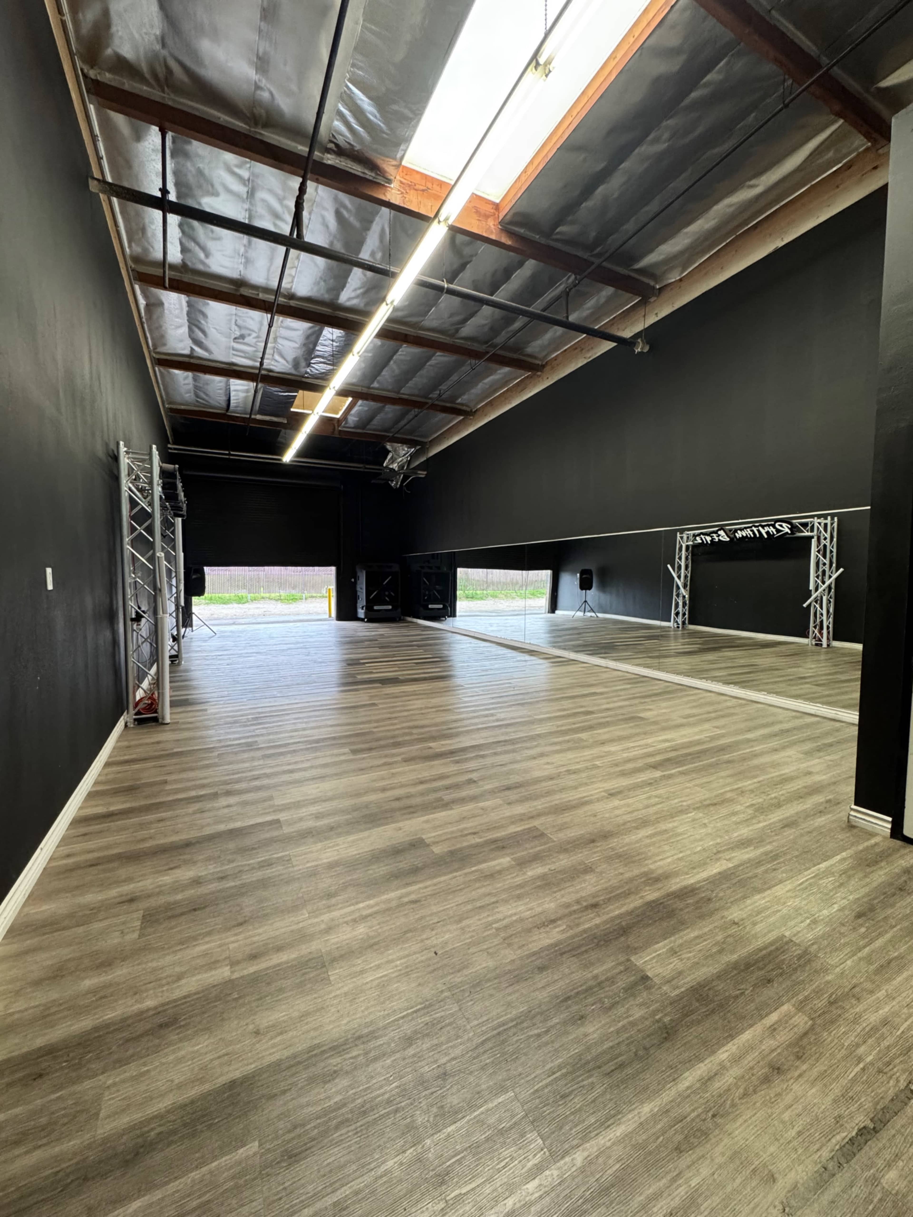 The image shows a spacious, empty studio with black walls, wooden flooring, and a high ceiling.