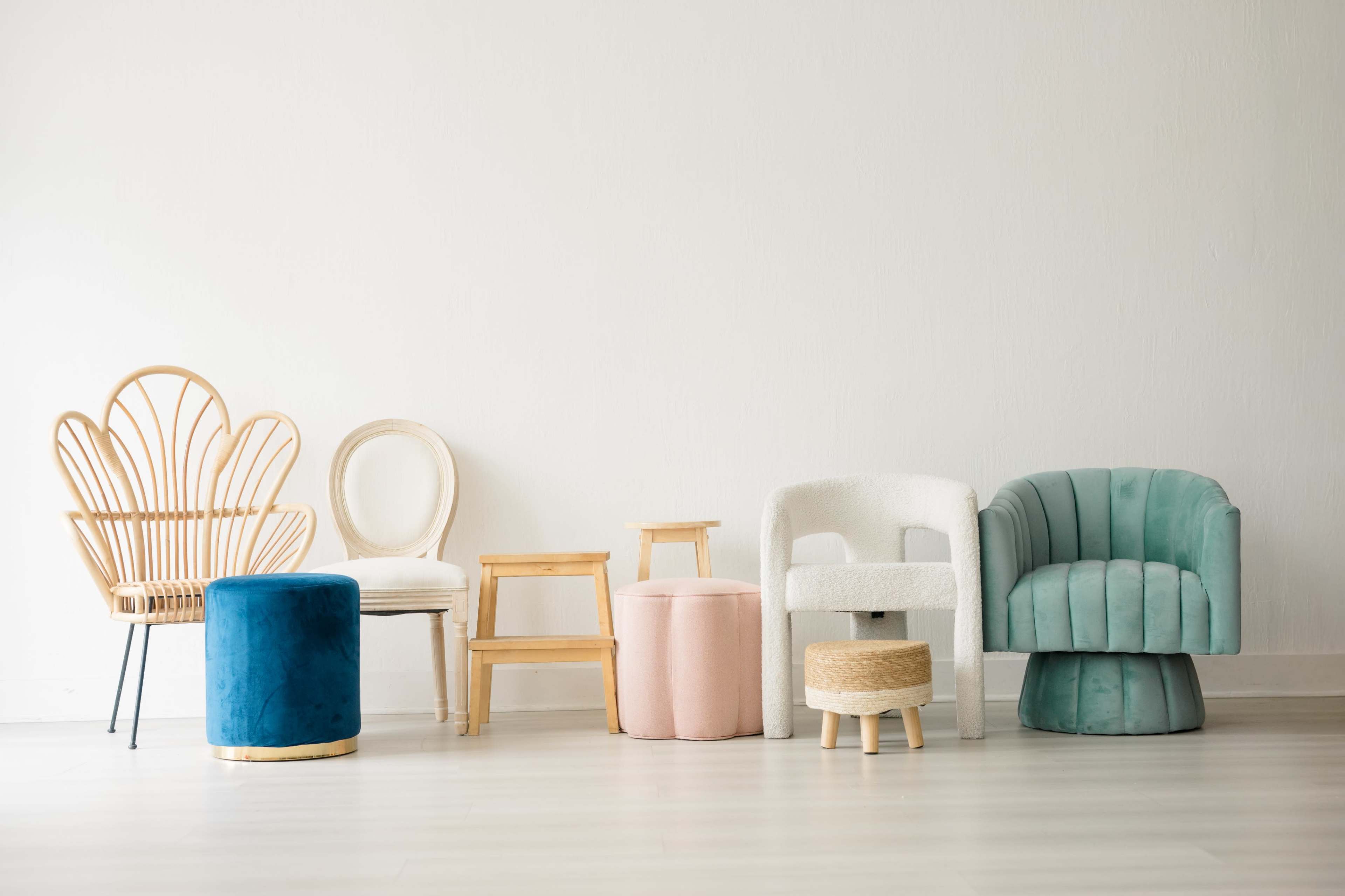 The image features a row of various styled chairs and stools, including a rattan chair, a white upholstered chair, and a velvet ottoman, against a plain wall.