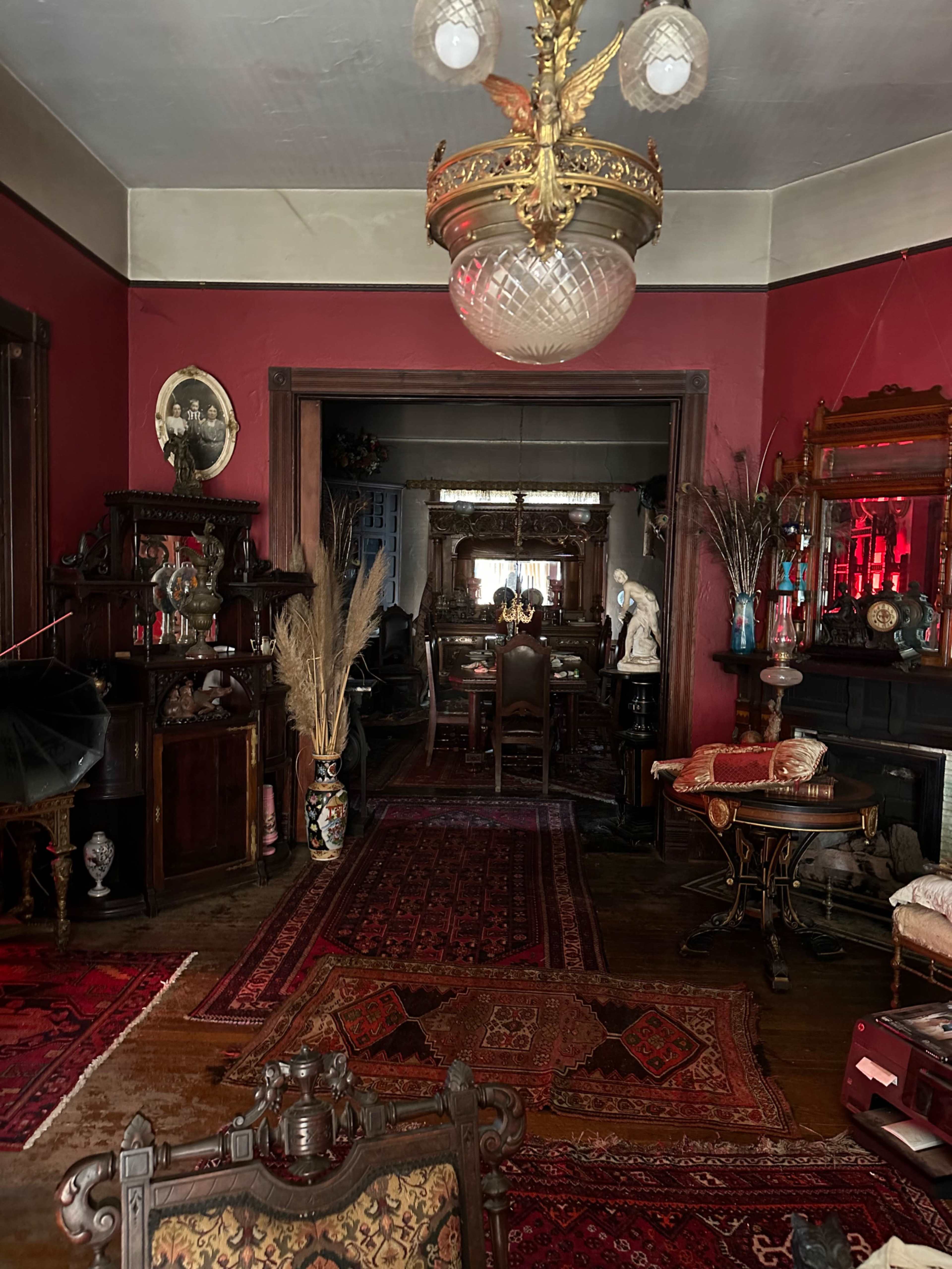 A vintage room with deep red walls, ornate furniture, and an elaborate chandelier, creating a richly decorated space.