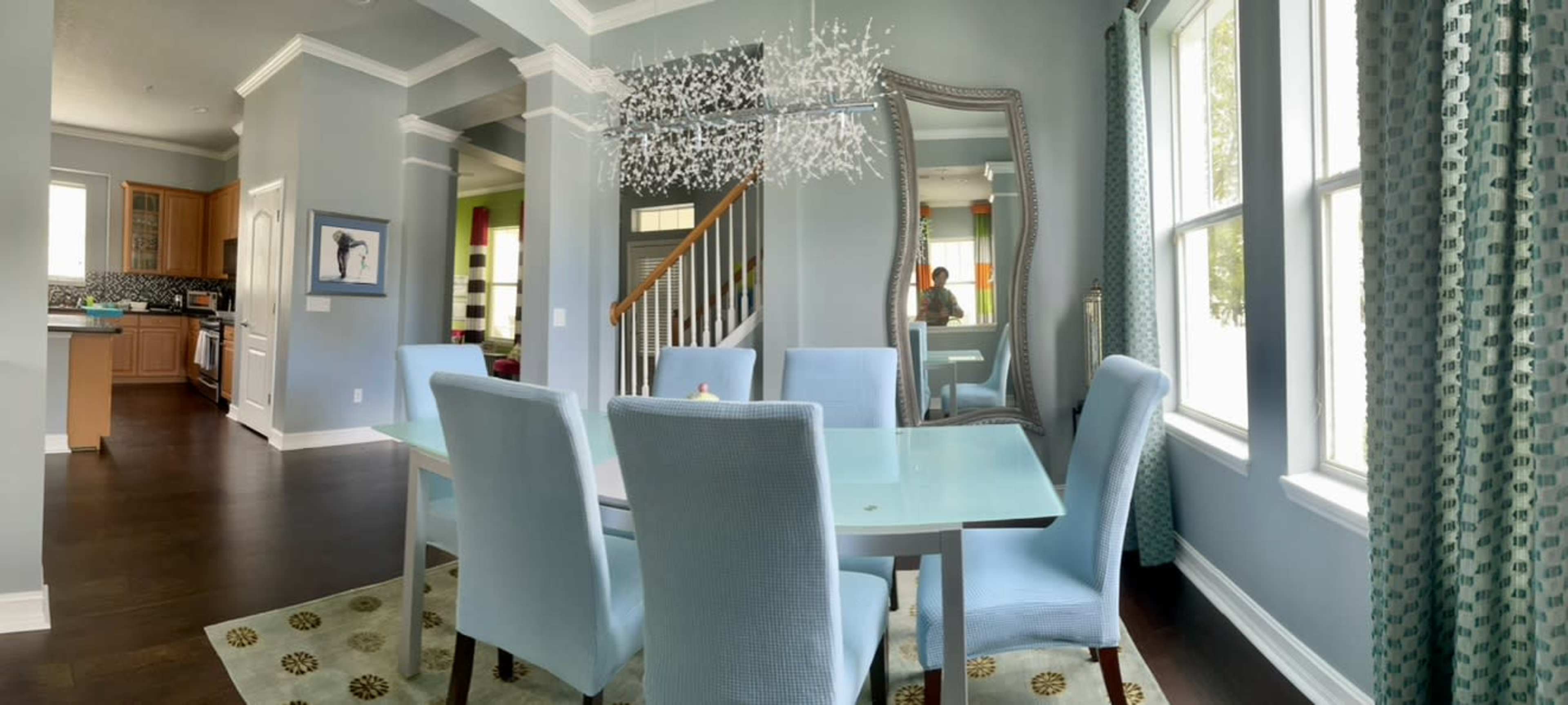 A dining area with a light blue table and chairs, a large mirror, and large windows allowing natural light to fill the space.