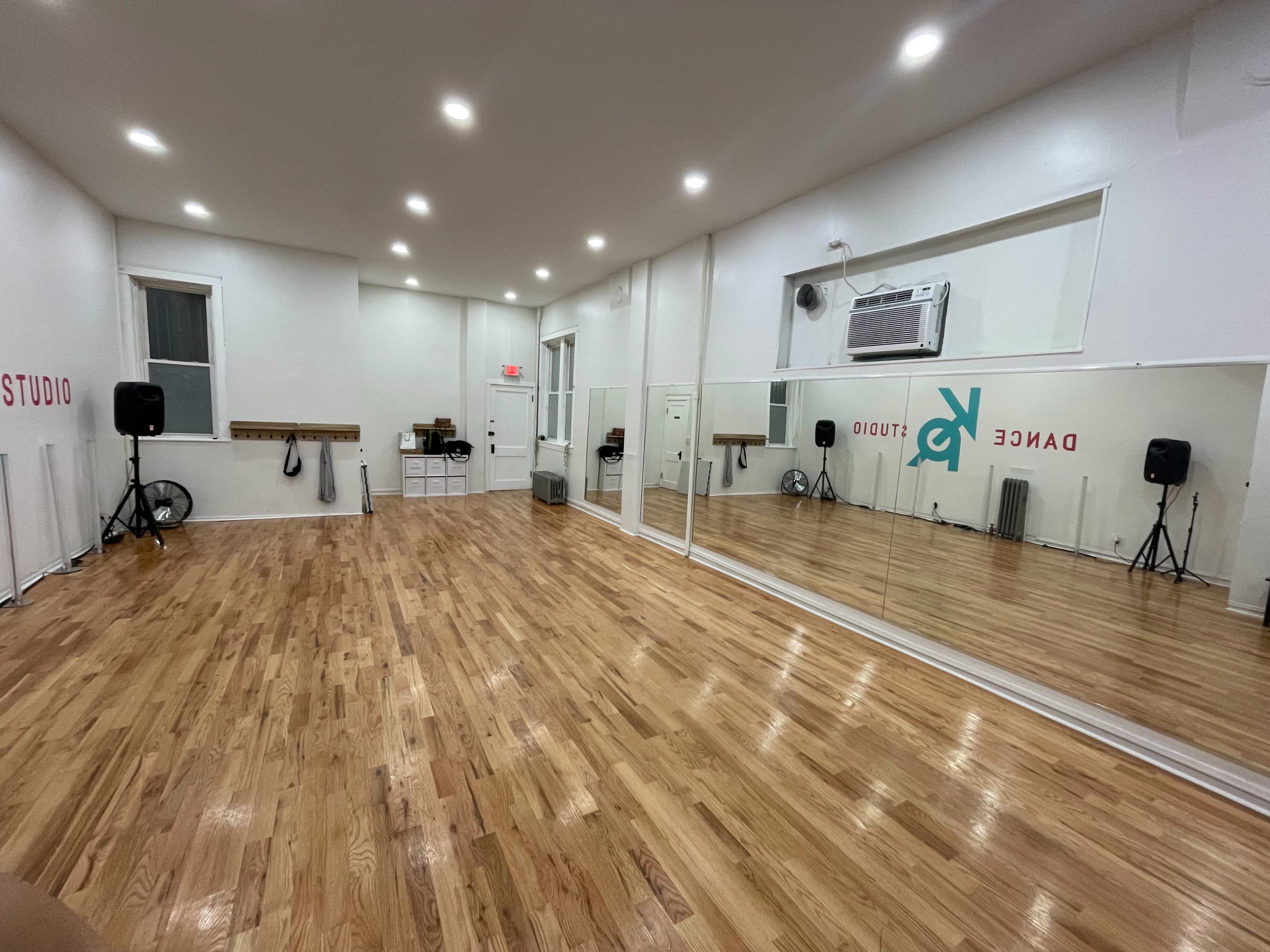 A spacious dance studio featuring hardwood flooring, mirrored walls, and ample lighting.