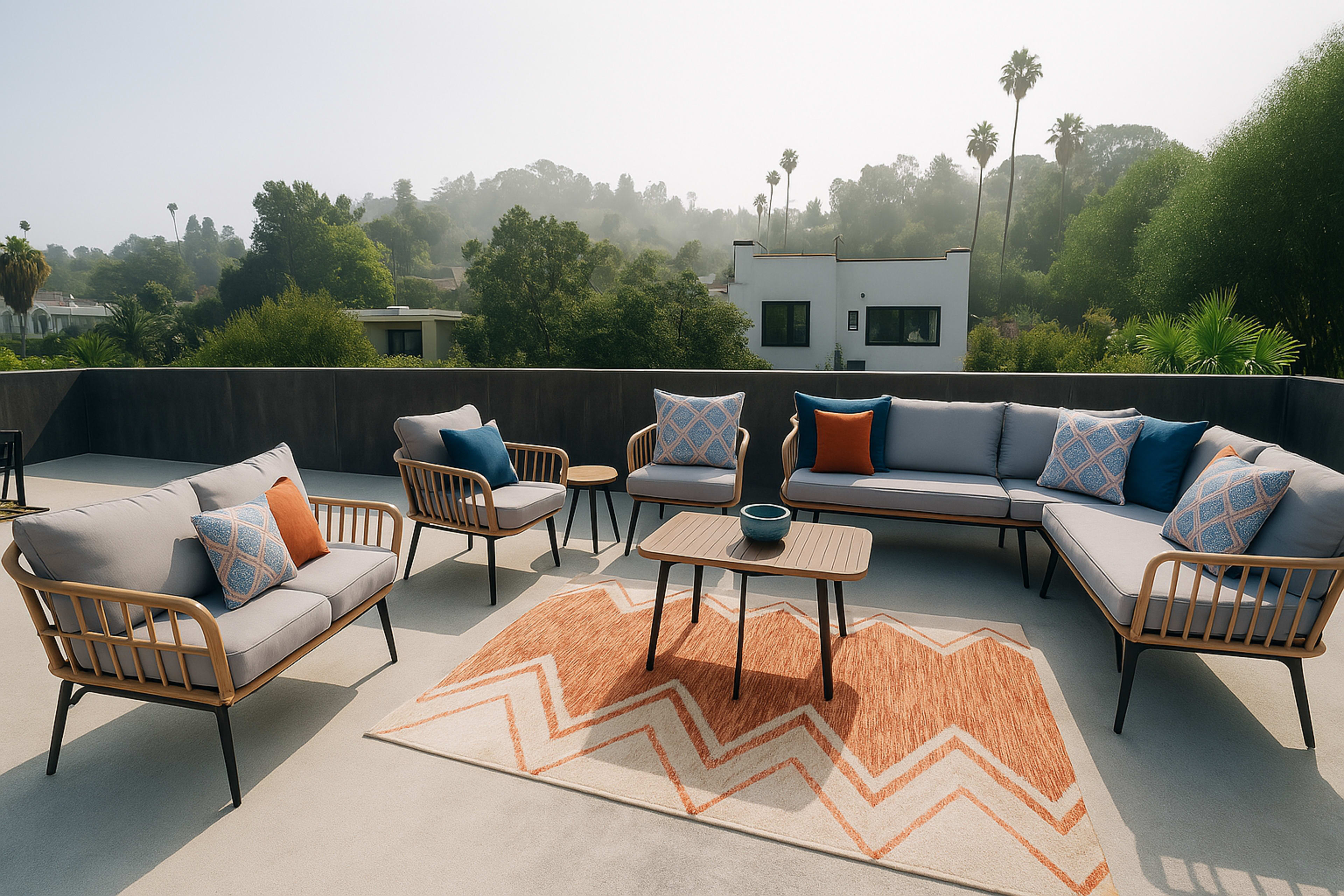 A modern outdoor seating area features a sectional sofa, armchairs, and a coffee table on a patio with a view of palm trees and hills.
