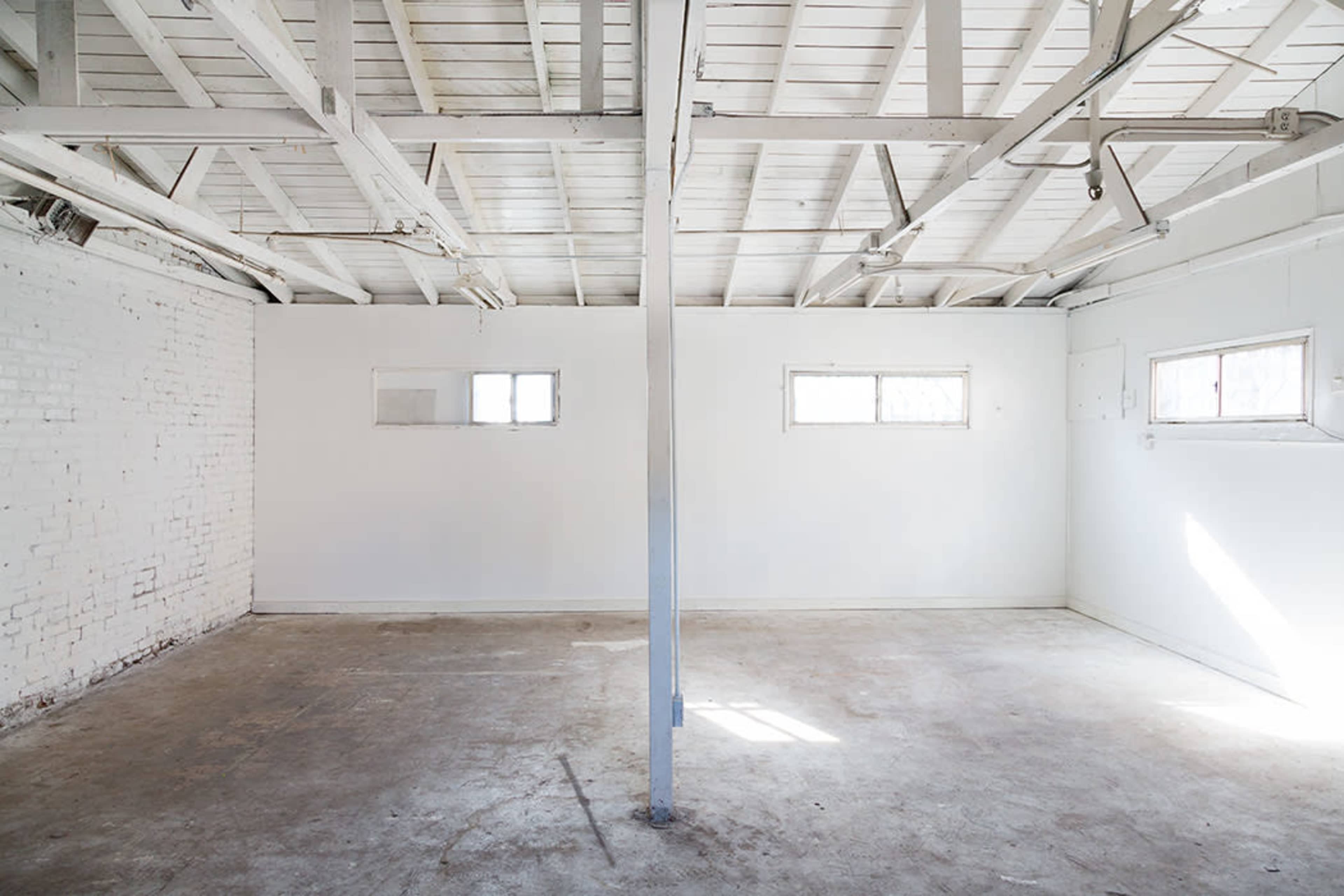 The image shows an empty, well-lit room with white walls, a concrete floor, and two small windows.