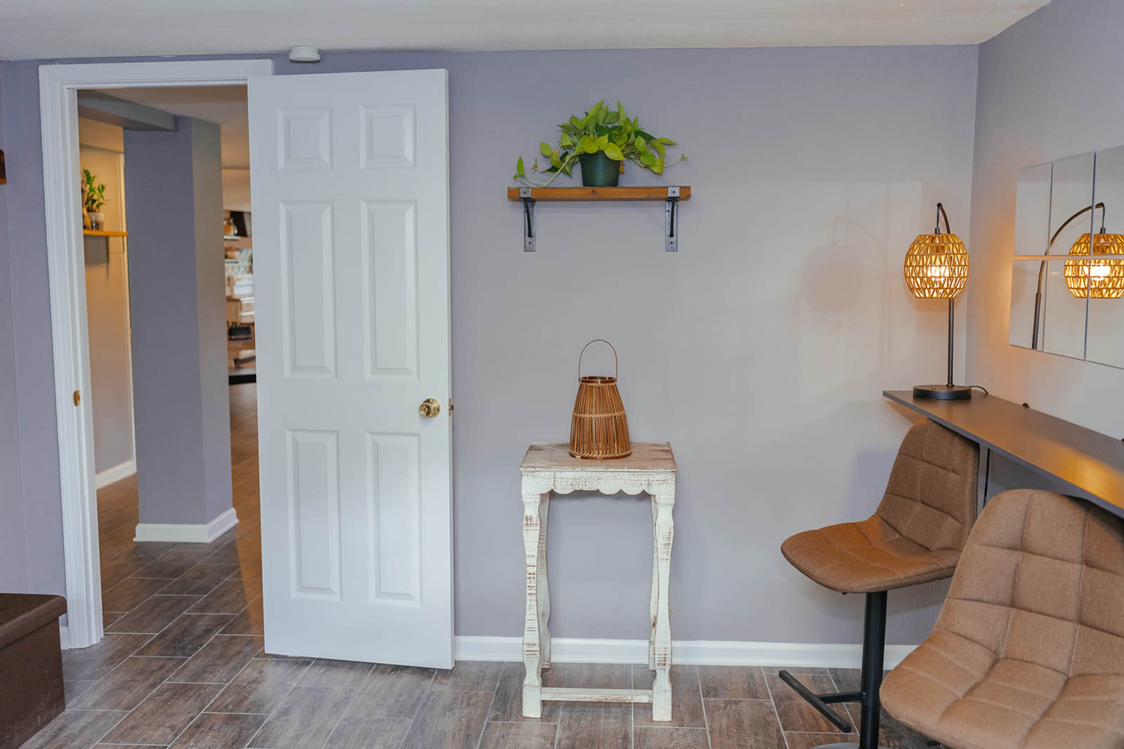 A minimalist room with a door, a small table, two chairs, and wall-mounted shelves featuring a plant and decorative lighting.