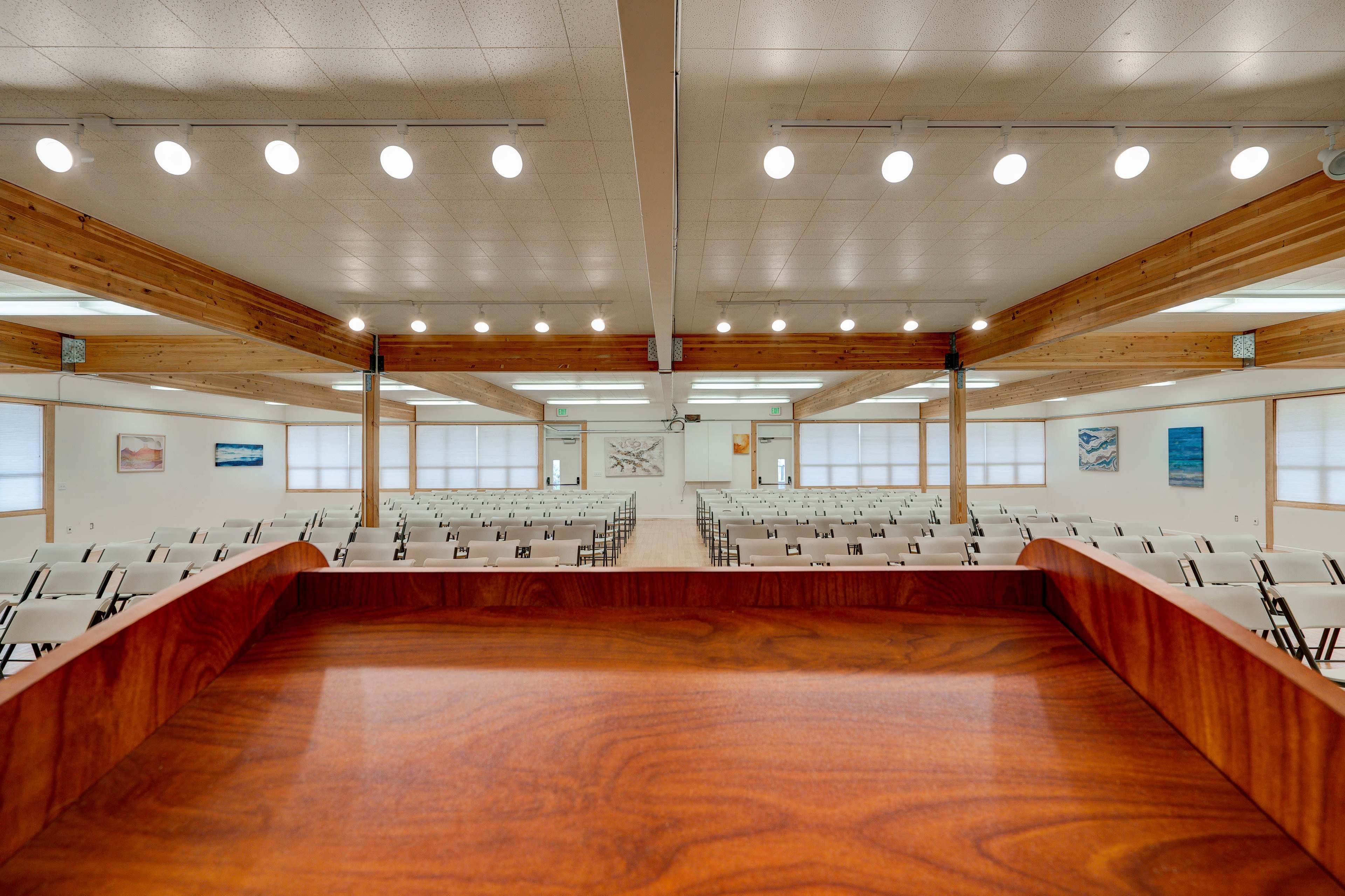 A large, empty assembly hall with rows of chairs facing a podium, illuminated by overhead lights.