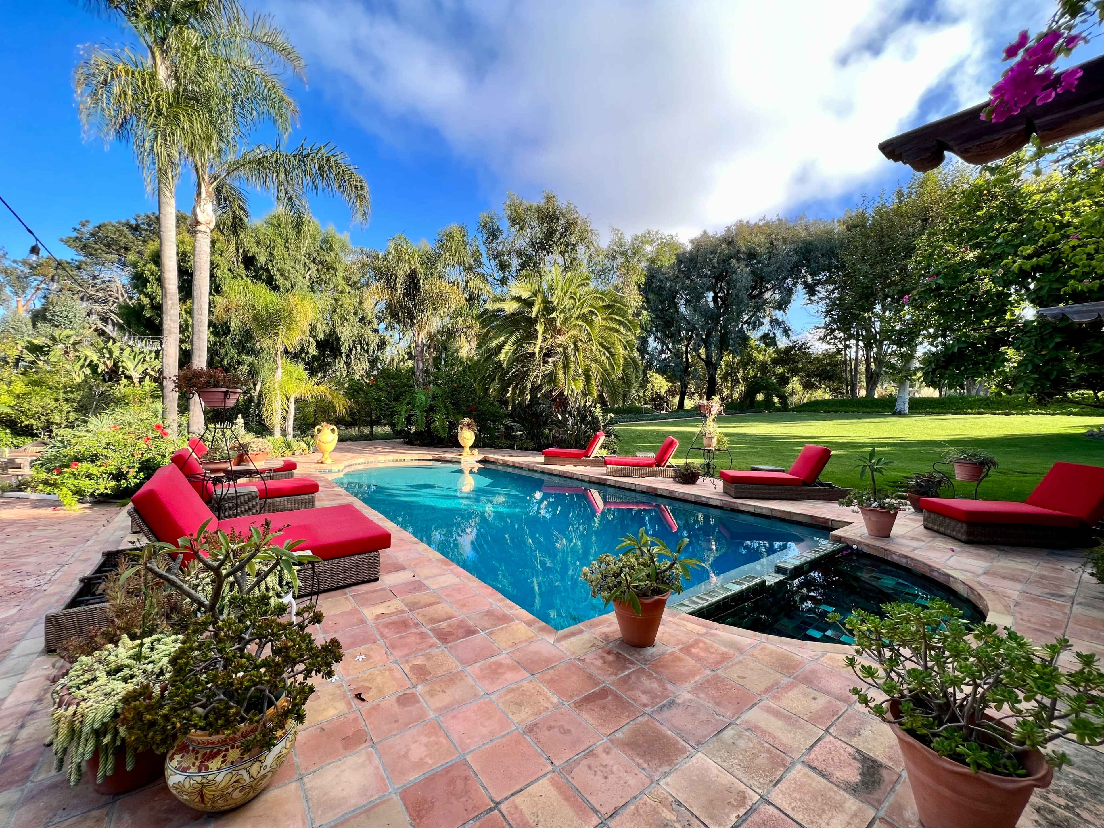 A swimming pool surrounded by red loungers and lush greenery in a residential backyard.