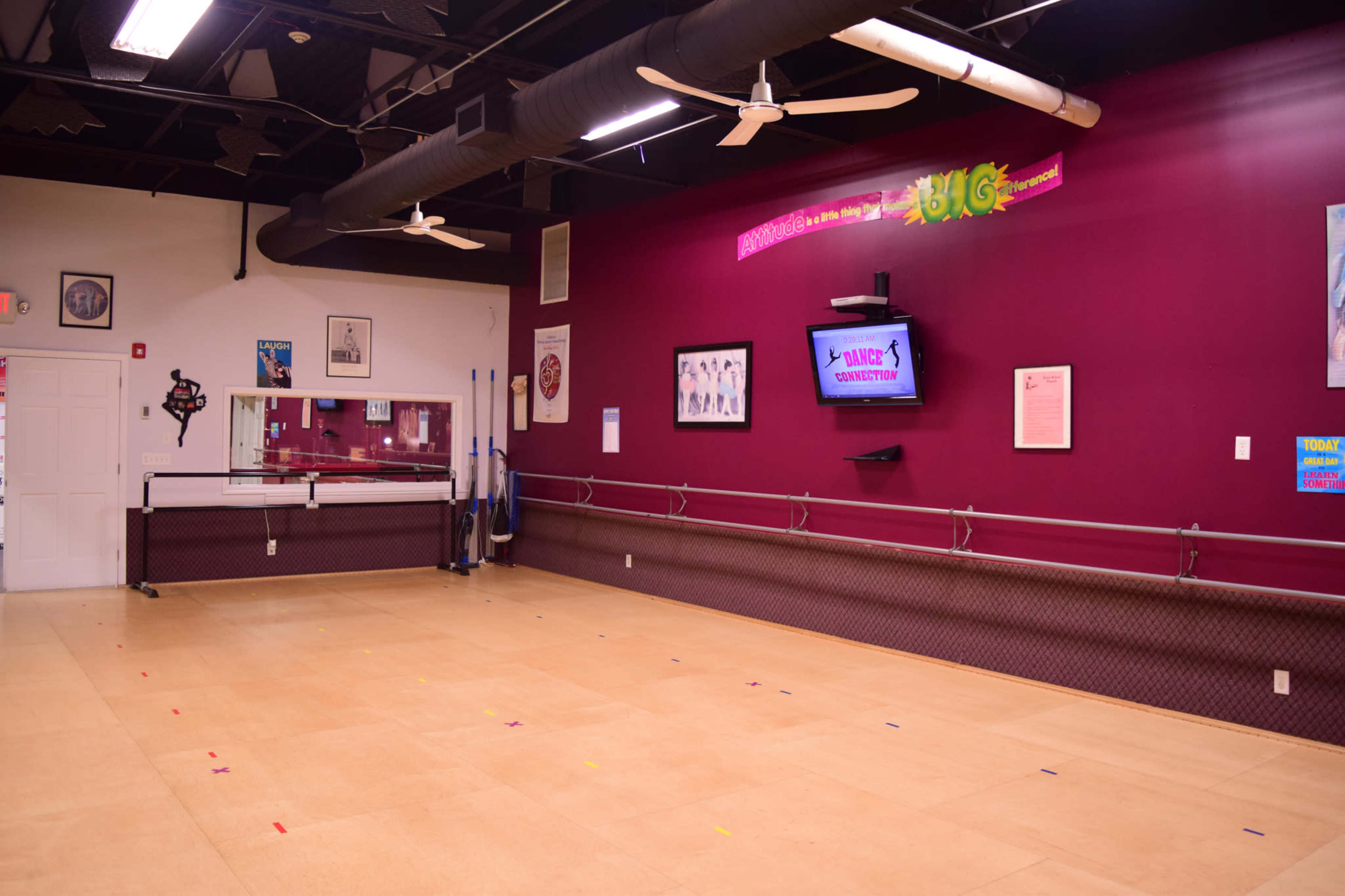 An empty dance studio with wooden floors, mirrors, and a television mounted on a purple wall.