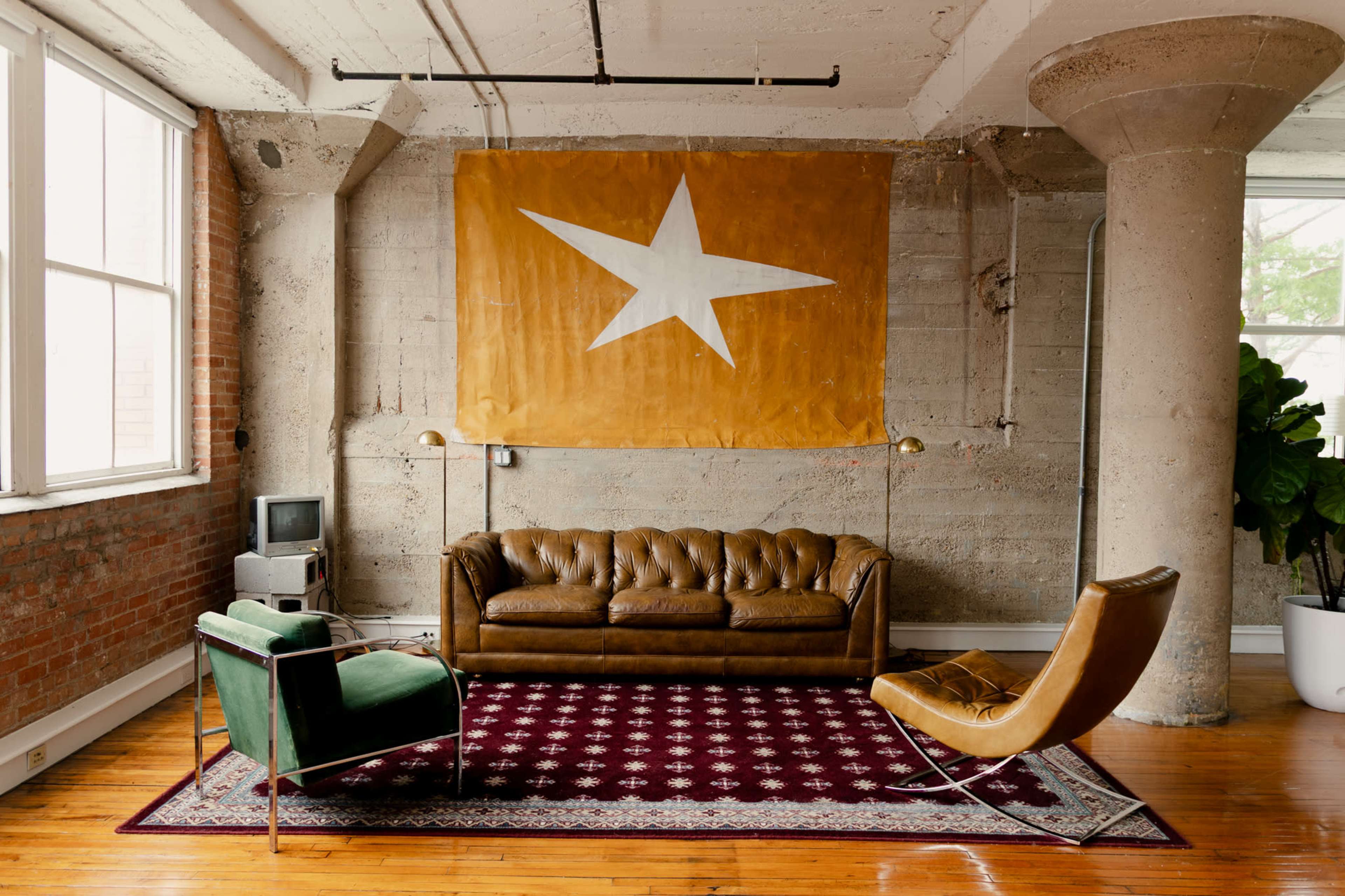 The image shows a spacious interior with a brown leather sofa, a green armchair, and a modern chair, accented by a large yellow banner featuring a white star on the wall.