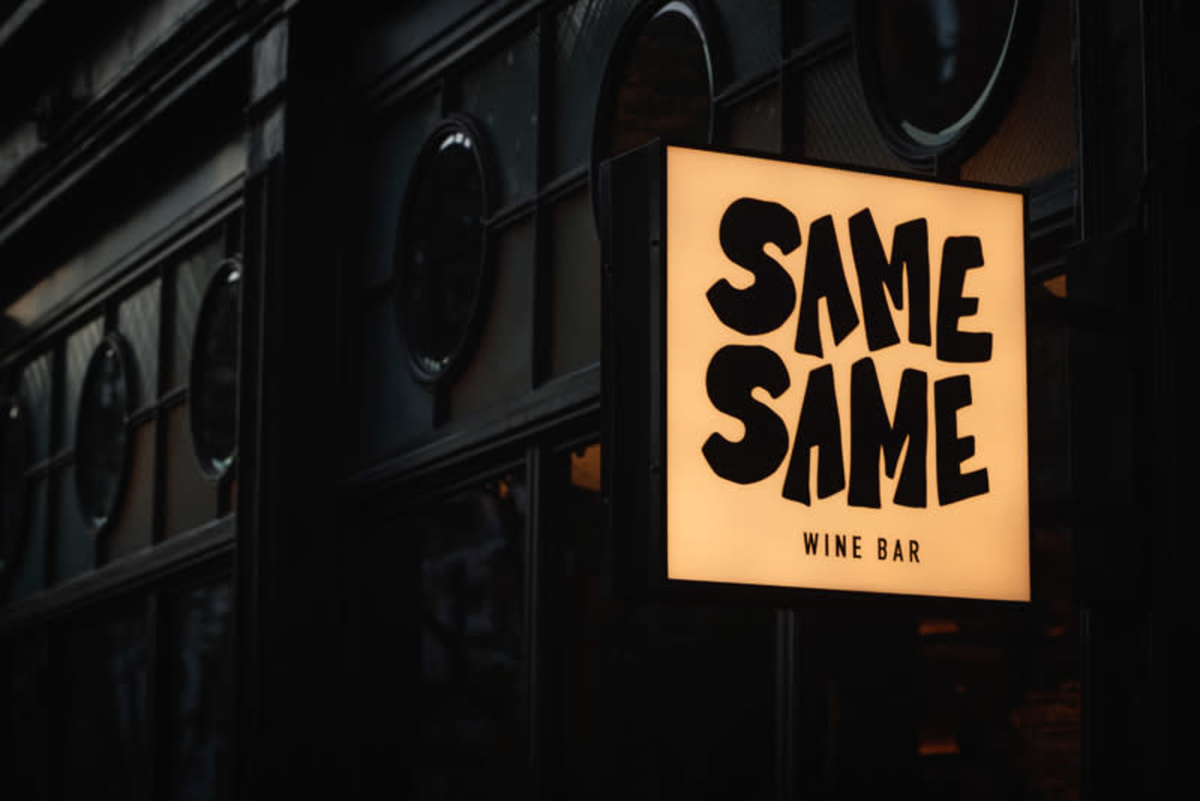 A illuminated sign displays the name "SAME SAME" with the words "WINE BAR" underneath.