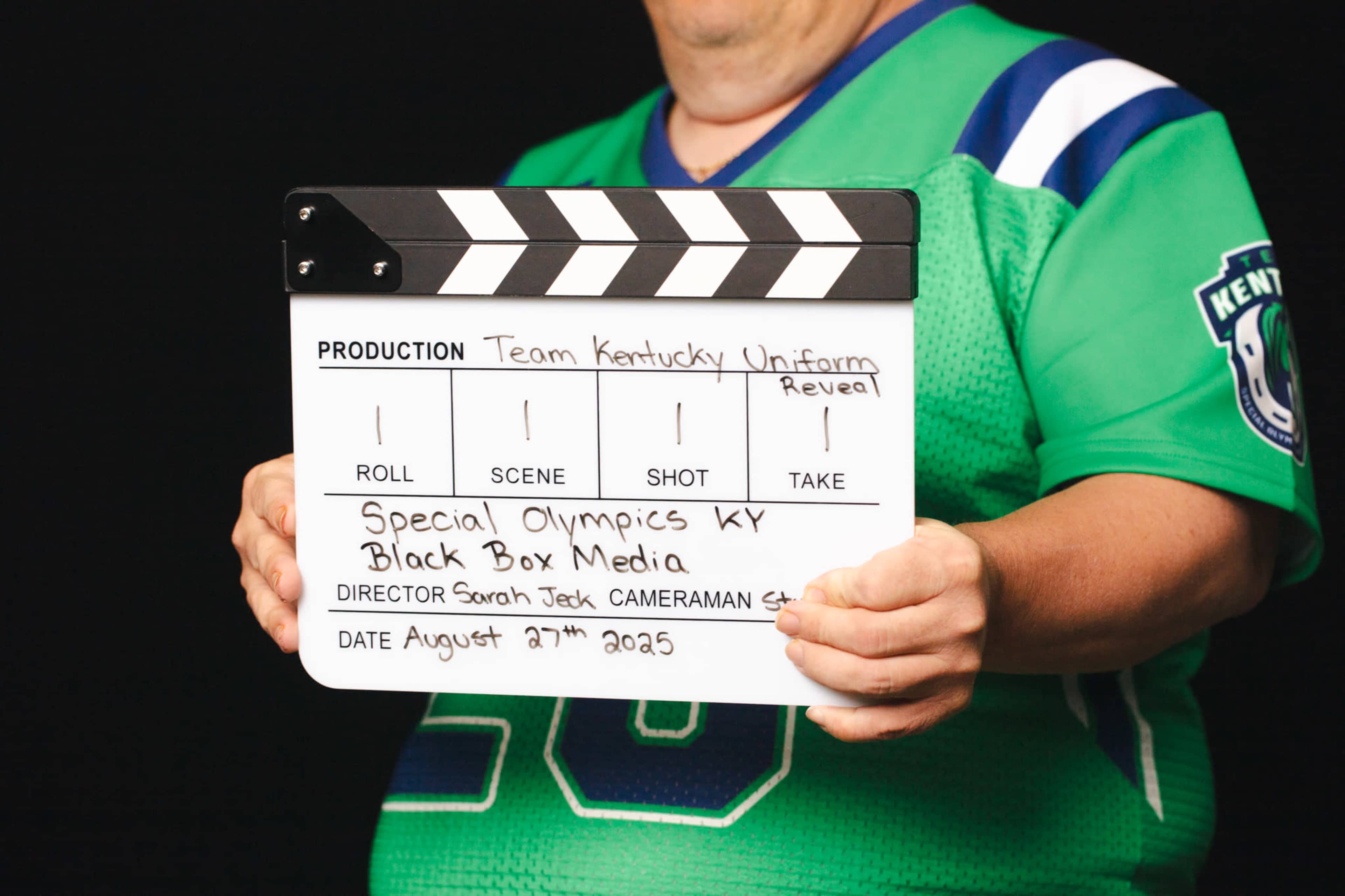 A person holds a movie clapperboard with production details for a "Team Kentucky Uniform Reveal" for Special Olympics Kentucky dated August 27, 2025.