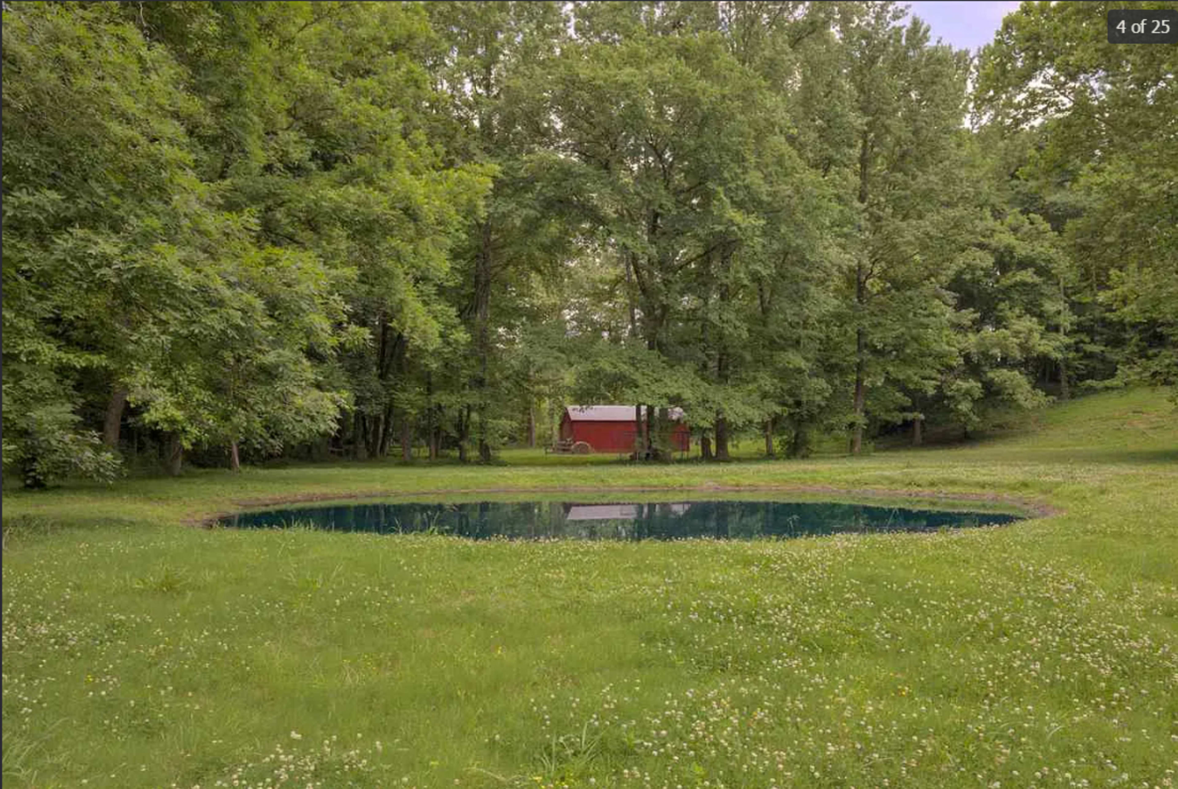 A red barn is visible in the background, surrounded by tall trees and a circular pond in the foreground.