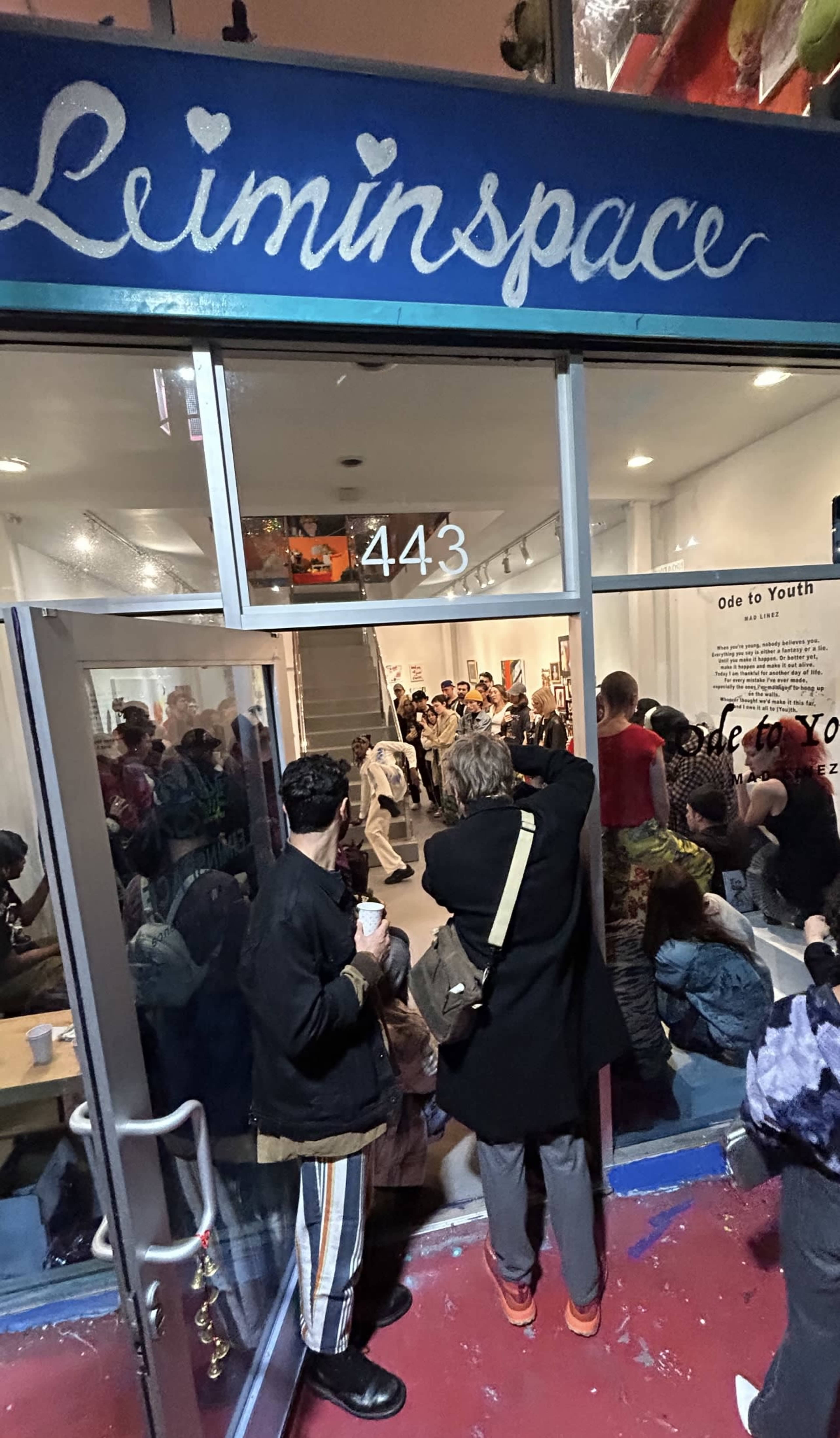 The image shows a lively art gallery event called "Ode to Youth," with a crowd of people gathered inside and outside the gallery's entrance.